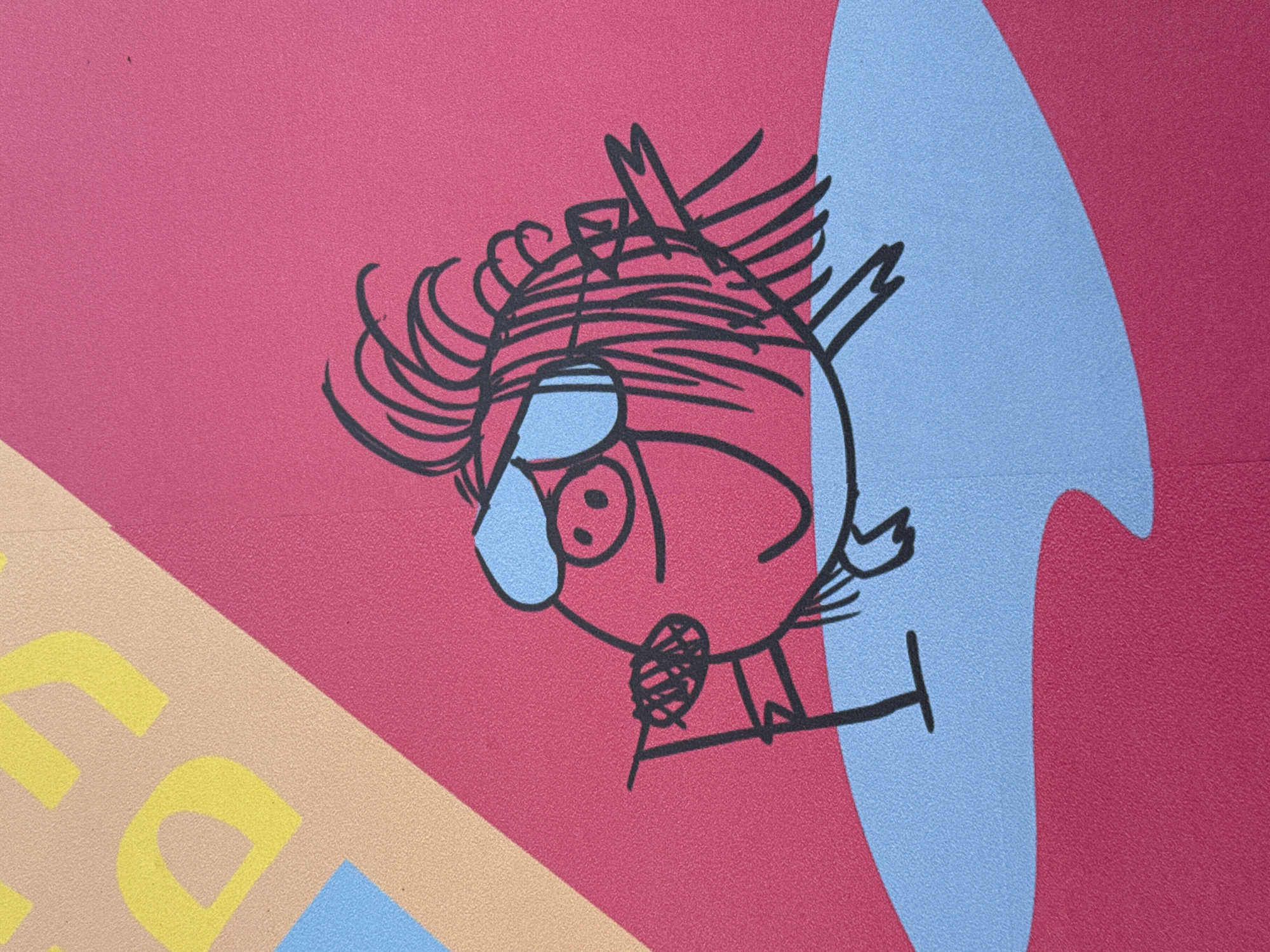 The image depicts a whimsical, cartoon-like drawing of a bird with exaggerated features, sketched in black lines on a colorful background. The bird has a rounded body, spiky feathers on its head and tail, and a singular large eye behind a blue-tinted goggle or visor. It appears to be perched or standing on a stylized 'T' shape.
The background is composed of flat blocks of color: red, light blue in the shape of a teardrop or flame, tan, and yellow. The colors are solid and uniform.
The location of the image is in Saint Petersburg, Russia.
