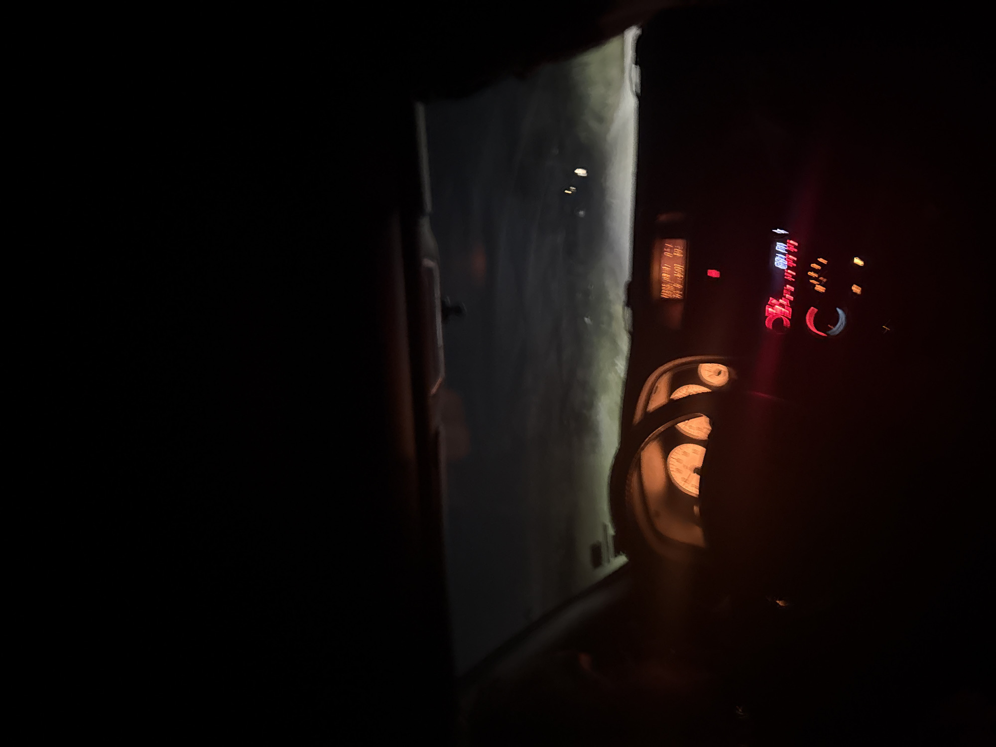 A nighttime view from inside a car. The illuminated dashboard and speedometer are visible. Through the windshield, the road ahead is dimly lit. It's not possible to determine the exact location in Elhovo, Bulgaria without more information. No people are clearly visible.