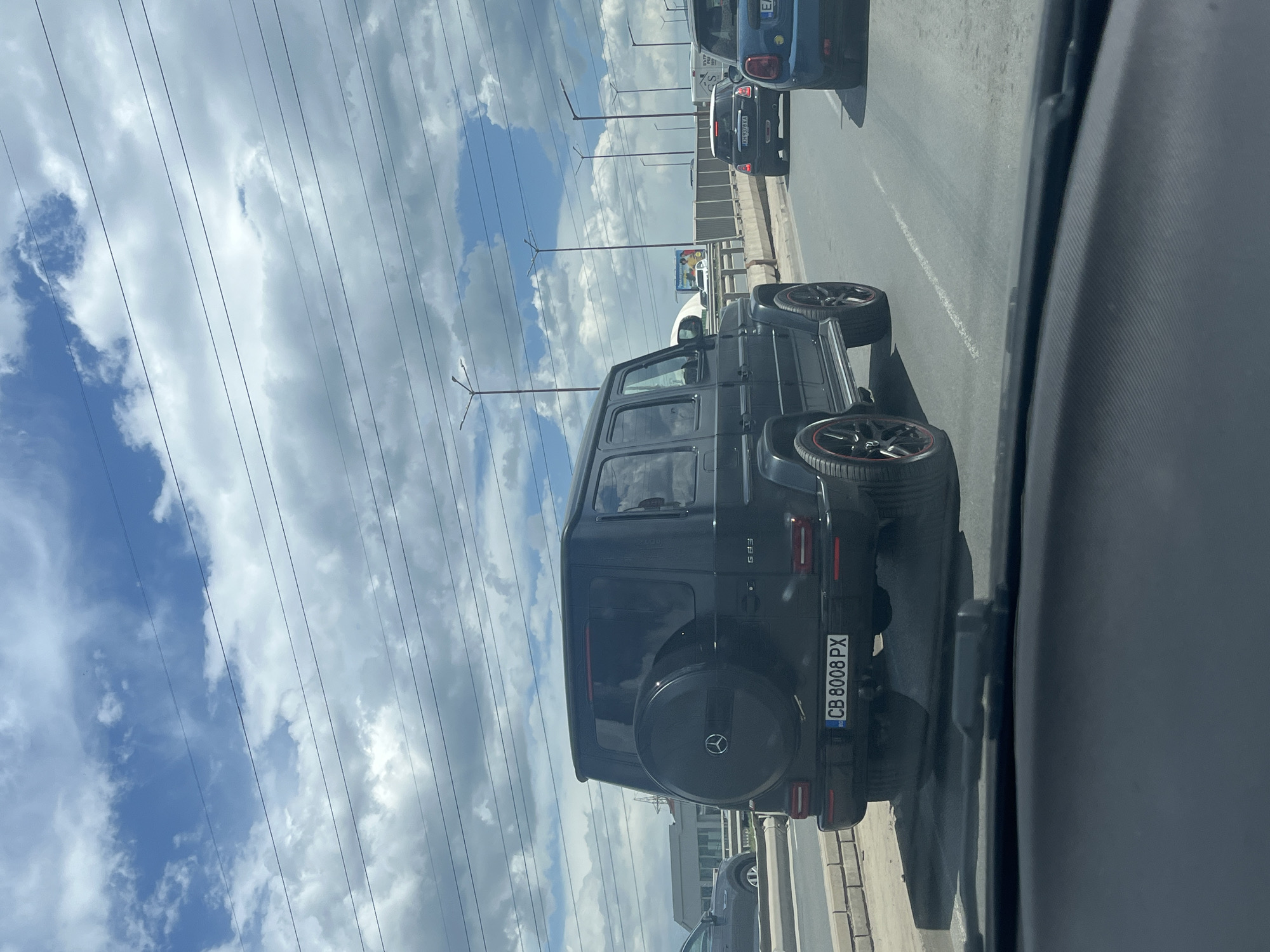 The image shows a black Mercedes-Benz G-Class (G63) with Bulgarian license plate CB 8008 PX driving on a road. The photo appears to be taken from inside another vehicle, looking out at the G-Class. The sky is cloudy. Based on the vehicle registration code "CB", this image was most likely taken in the city of Sofia, Bulgaria. Other vehicles are visible in the background.