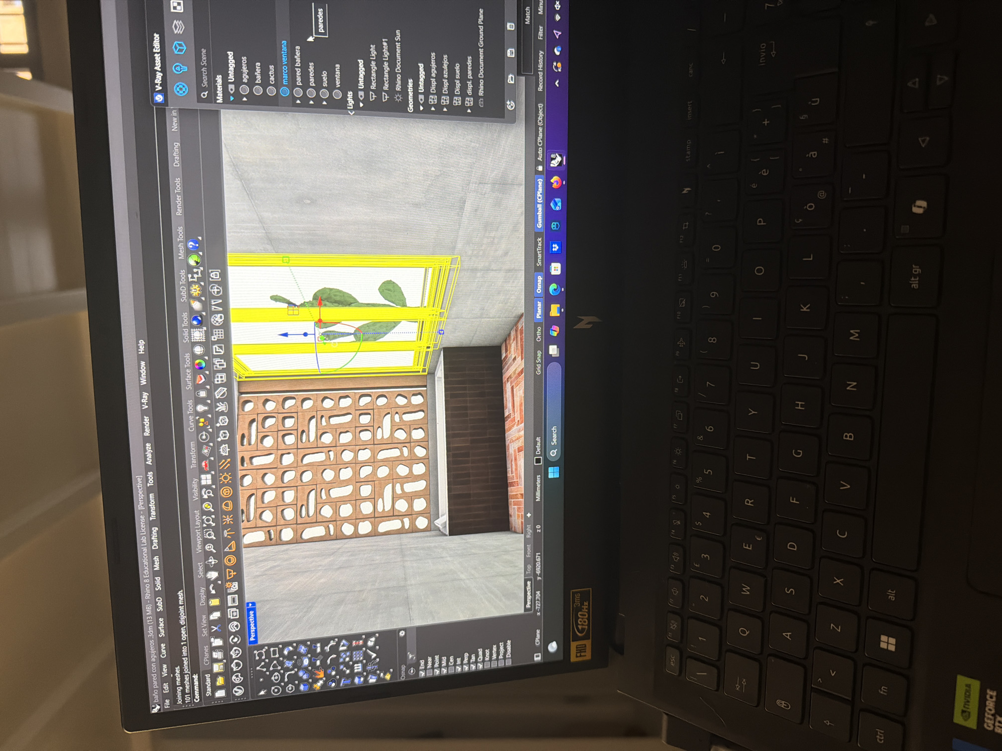 The image shows a computer screen displaying a 3D architectural rendering within Rhino 8 software. The rendering depicts an interior scene, seemingly a bathroom, with various architectural details.
Objects: The scene includes elements such as walls, a window with a cactus, and a decorative wall with geometric cutouts. Materials are labeled in the V-Ray Asset Editor as "agujeros" (holes), "bañera" (bathtub), "cactus", "marco ventana" (window frame), "pared bañera" (bathtub wall), "paredes" (walls), "suelo" (floor), and "ventana" (window). Lighting is managed with a "Rectangle Light" and "Rhino Document Sun".
Software: The software visible is Rhino 8, as indicated in the title bar of the window. V-Ray is being used as the rendering engine.
Environment: The environment appears to be a studio or workspace based on the presence of the laptop on a surface.
Location: The image doesn't provide enough information to specify the location as the city of Milan in Italy.
The laptop keyboard is visible in the foreground, showing a typical layout with language-specific characters (e.g., "è," "ò," "à," "ù"). The laptop has an NVIDIA GeForce RTX sticker, indicating its graphics capabilities.