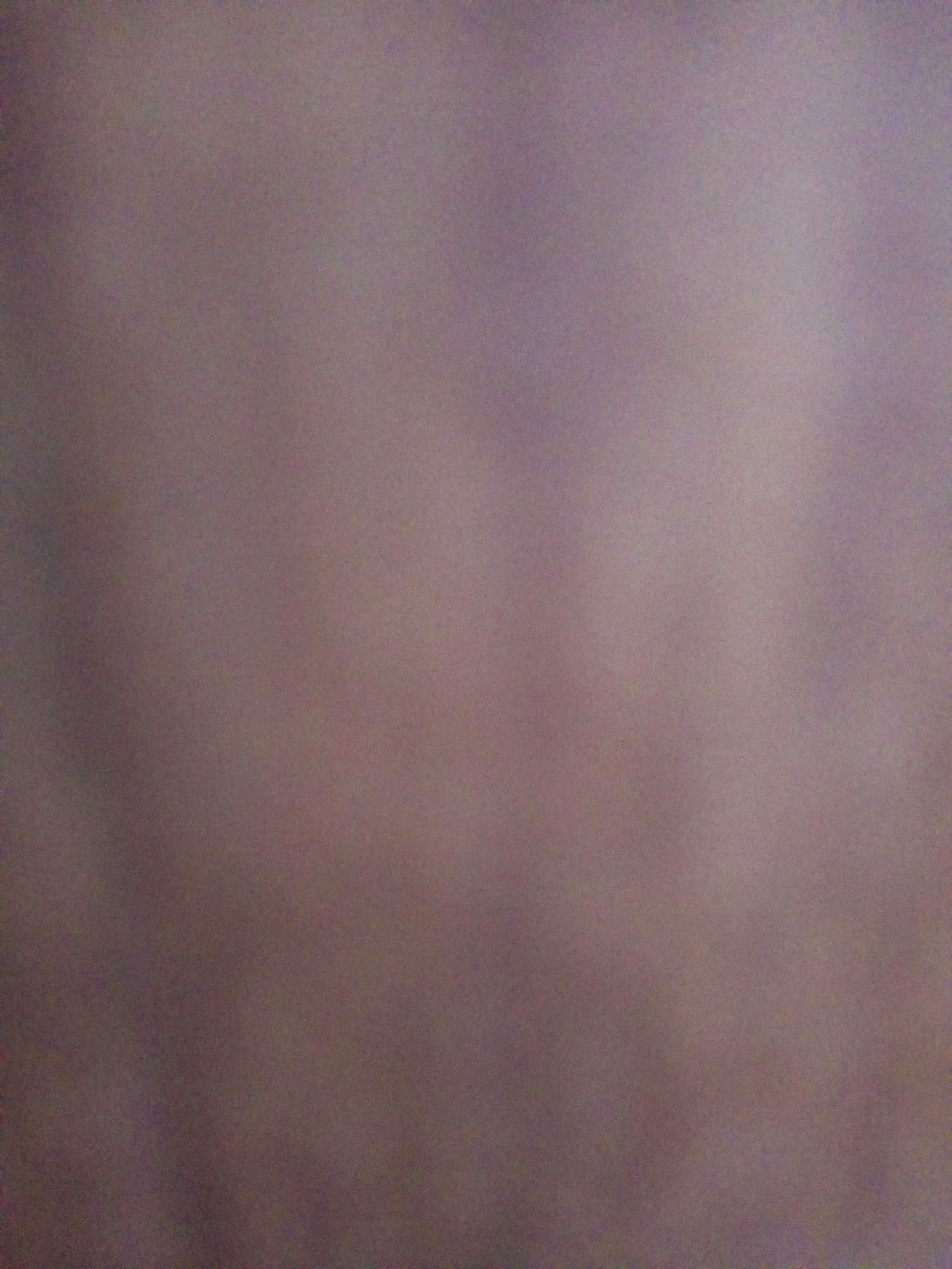 The image is a blurred, abstract photograph with a muted color palette. It appears to be a close-up shot of a textured surface, possibly fabric or paper, with soft variations in light and shadow. There are no discernible objects, people, or any recognizable features of the city of Batam, Indonesia, or any urban environment. The image lacks any specific details that would allow for a forensic or location-based description.