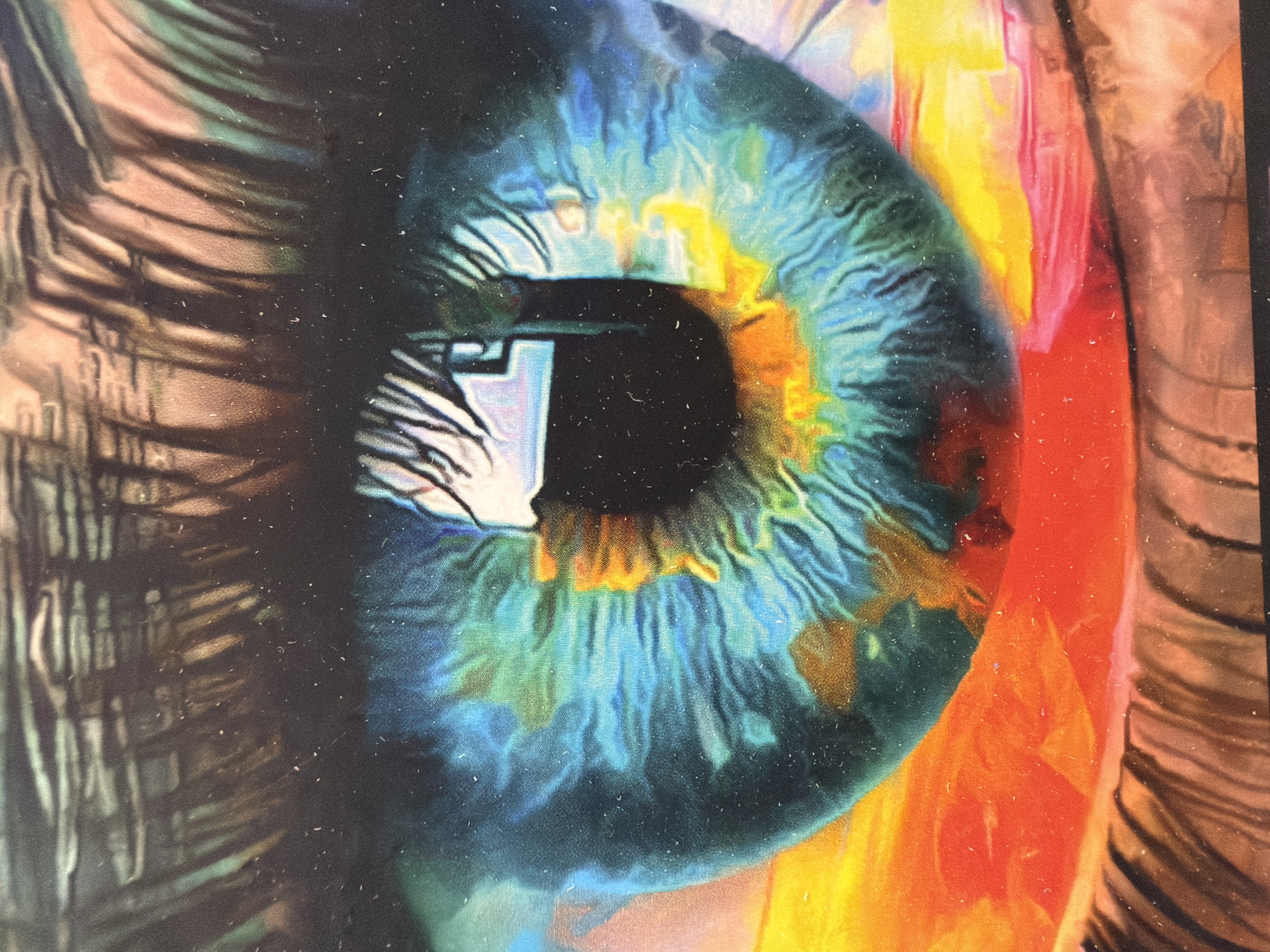 This is a close-up, artistic representation of a human eye, likely a painting or digital artwork. The iris is depicted in vibrant hues of blue, green, and yellow, with intricate details of its radial patterns and the pupil as a dark void. The eye appears to be looking towards the left of the frame, with reflections of light and possibly the surrounding environment visible on its surface, including what seems to be a rectangular object with white and blue tones.
To the left of the eye, abstract lines in shades of brown and grey suggest eyelashes or the outer edge of the eye socket, rendered in a textured, almost metallic style. To the right of the eye, large swathes of bright color, primarily oranges and yellows, along with some red and pink, create a vibrant, abstract background that could represent light, abstract shapes, or possibly other parts of the face, like the cheek or forehead. The overall impression is one of intense focus and a dreamlike, surreal quality due to the exaggerated colors and abstract elements. The artwork has a grainy texture, possibly due to the medium or a photographic effect, and small white specks are scattered across the surface, resembling dust or imperfections. There is no discernible text in the image. The setting and time of day are not indicated, but the intense lighting and vibrant colors suggest an artificial or highly stylized environment. The emotion conveyed is one of deep contemplation or perhaps awe.