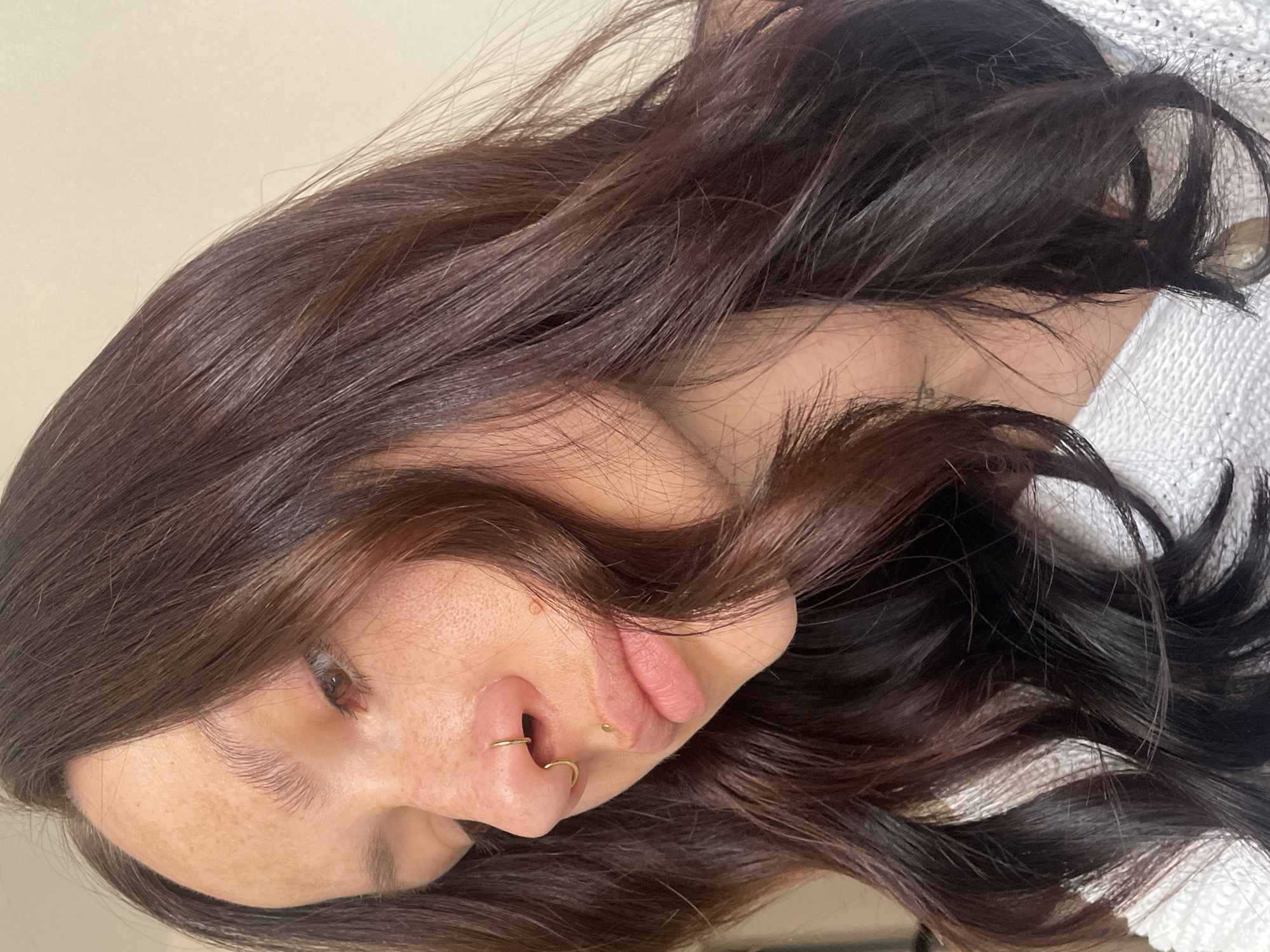 The image shows a woman with dark brown hair and fair skin. She has a gold ring piercing in each nostril and a mole on her upper lip. She is wearing a white knitted sweater. There is no indication that the image was taken in Izhevsk, Russia.