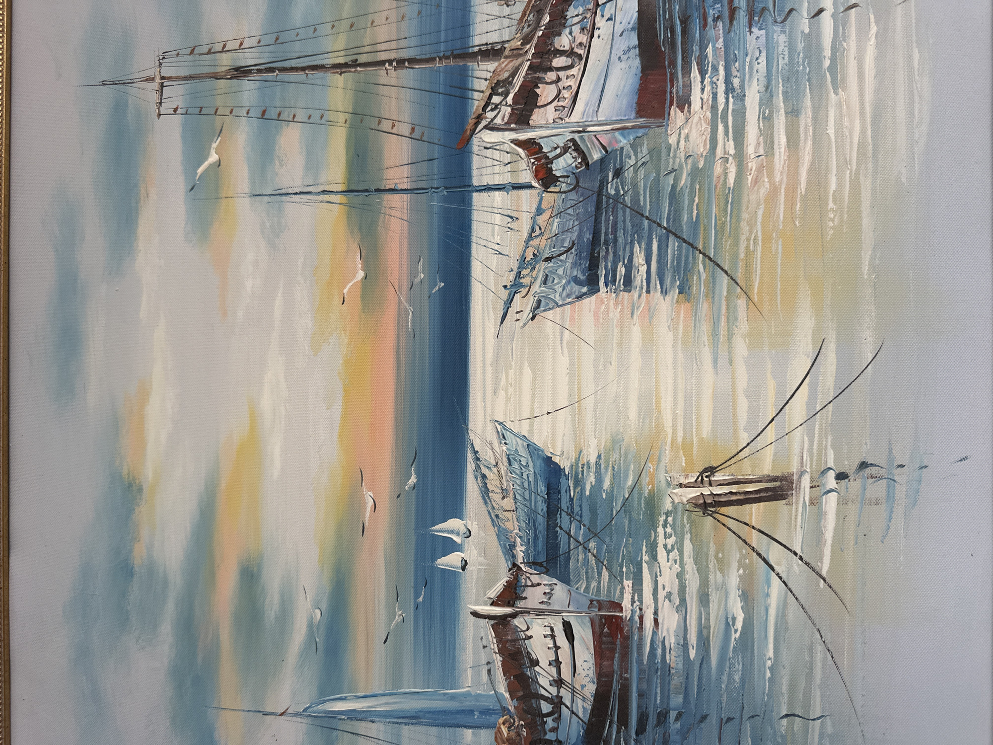 This is a painting of sailboats at anchor in calm water. The sky is depicted with soft clouds in shades of blue, white, and hints of orange and pink, suggesting either sunrise or sunset. Several seagulls are painted in flight across the sky. In the foreground, several sailboats are moored. One large sailboat with a tall mast and rigging dominates the right side of the composition. Another sailboat with a blue hull is positioned to the left of it. In the distance, two smaller sailboats with white sails are visible. The water reflects the colors of the sky and the boats. The overall scene is serene and picturesque, with a focus on the interplay of light and water. This painting does not depict any specific location in Vilnius, Lithuania.