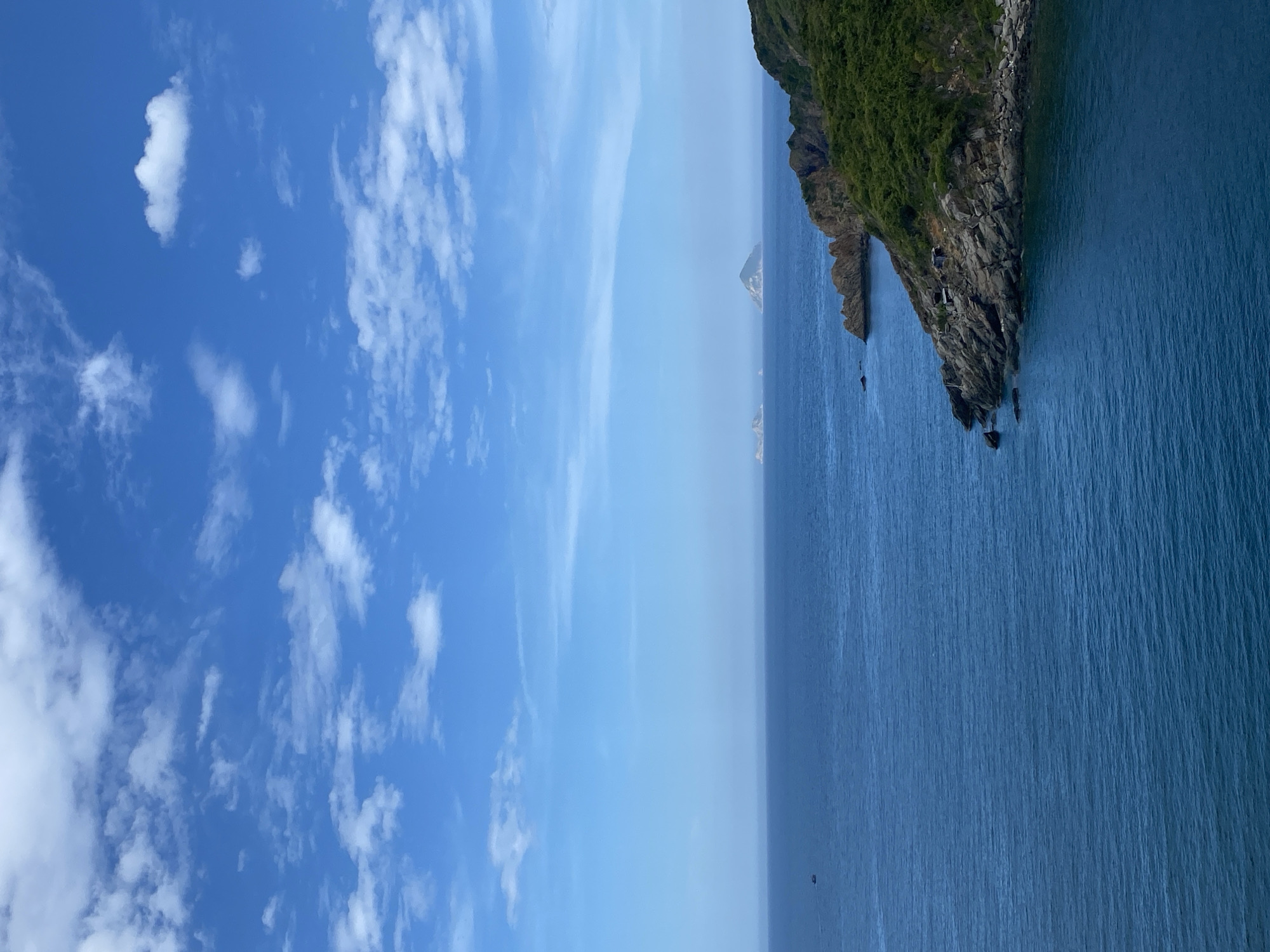 The image depicts a serene seascape with a vibrant blue sky dotted with scattered white clouds. In the distance, several small islands rise from the calm, deep blue ocean. The foreground features a rocky coastline covered with lush green vegetation. The overall scene suggests a tranquil, natural environment.
While the image provides a beautiful landscape, it does not contain any specific landmarks or identifying features that would allow for its precise location within the city of Nha Trang, Vietnam, to be determined. The presence of the ocean, islands, and rocky coastline are common geographical elements in coastal regions like Nha Trang.