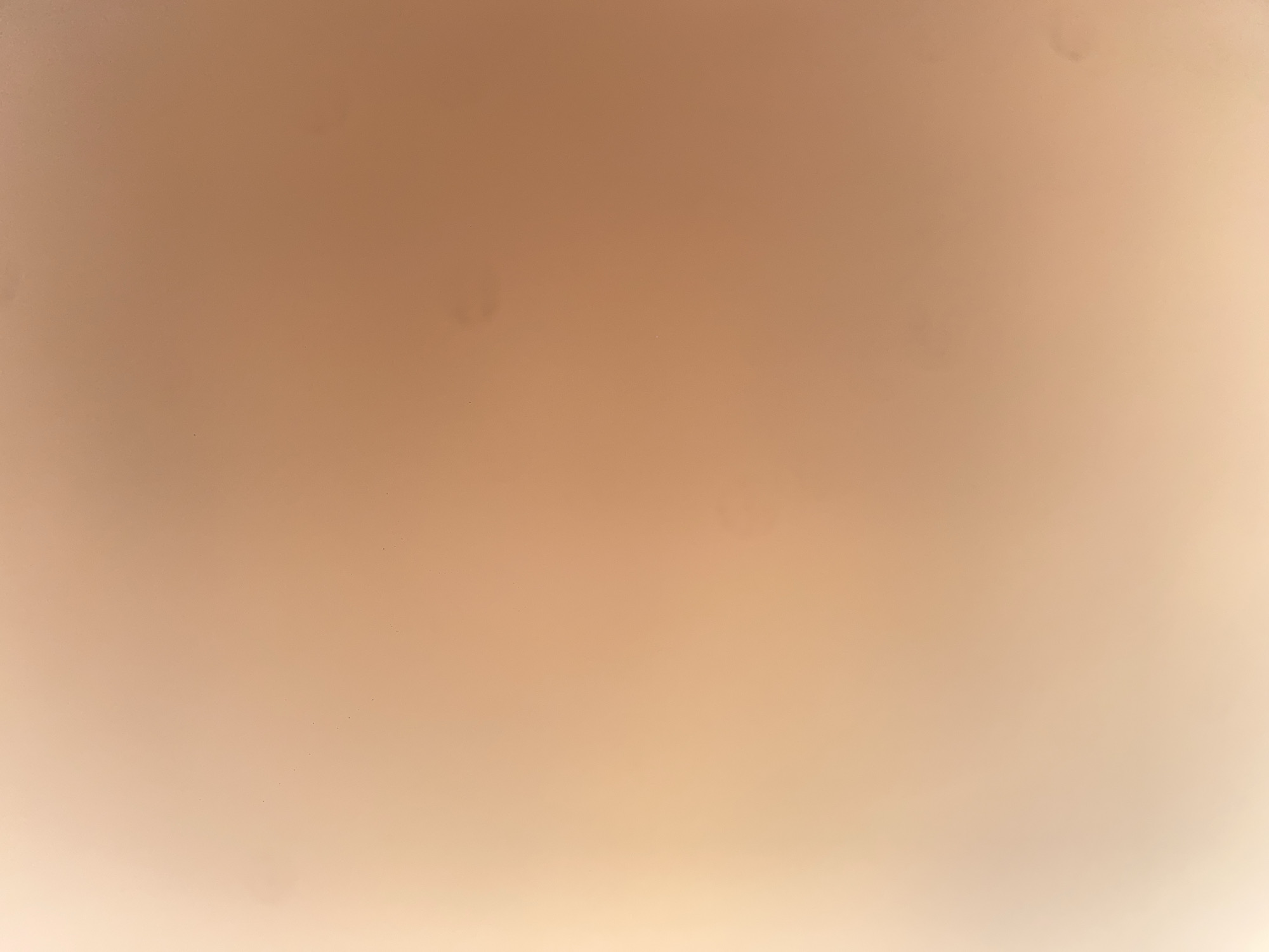 The image is an abstract, out-of-focus photograph with a warm, peachy-tan color gradient. The lighting is soft, creating a gentle transition from a brighter, lighter area on the left to a darker, more saturated area on the right. There are a few small, dark specks visible, which could be dust or imperfections in the image. The overall impression is one of softness and warmth, with no discernible objects or subjects in focus. The image does not contain any visual information that can be linked to the city of Ablanitsa, Bulgaria, or any specific location.