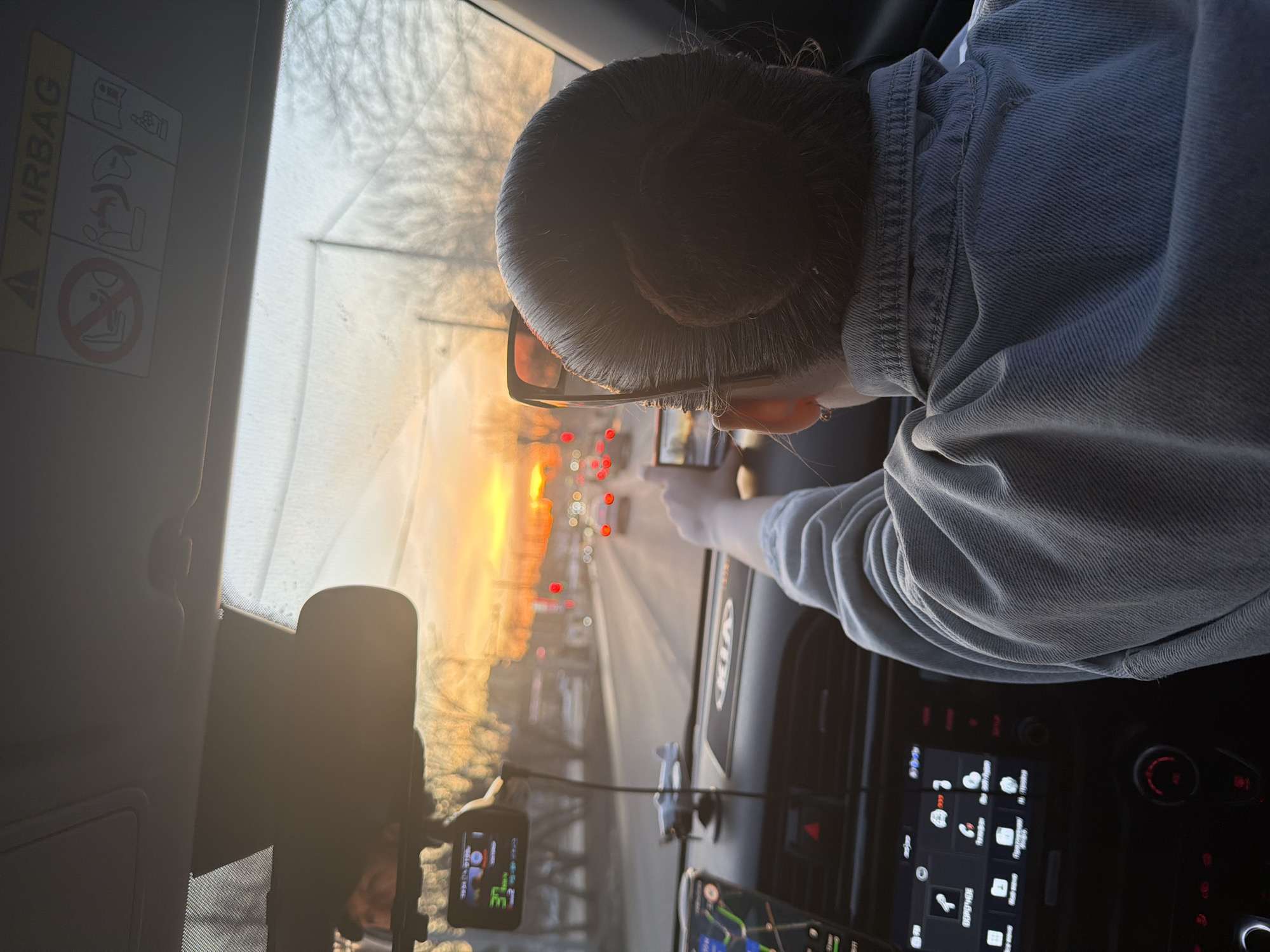 A person is in a car, pointing out the window at a traffic jam on a highway at sunset. The car interior is visible, including the dashboard and a GPS device. An "AIRBAG" label is visible on the sun visor. The city is Perm, Russia, indicated by the Cyrillic writing on the GPS device displaying a map of the area.