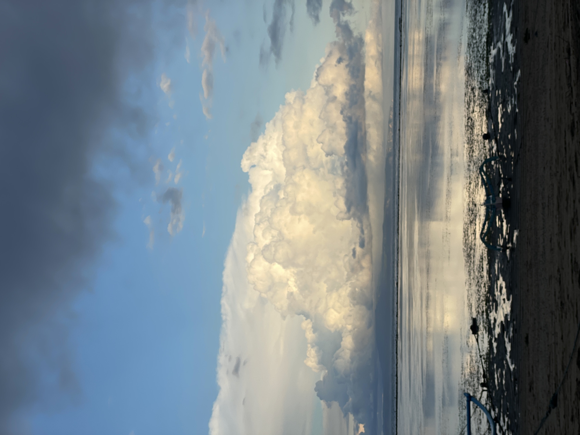 A cloudy day at Sanur Beach in Denpasar, Indonesia. The tide is low, exposing mud flats. A small, blue-trimmed boat rests on the beach in the right portion of the image.