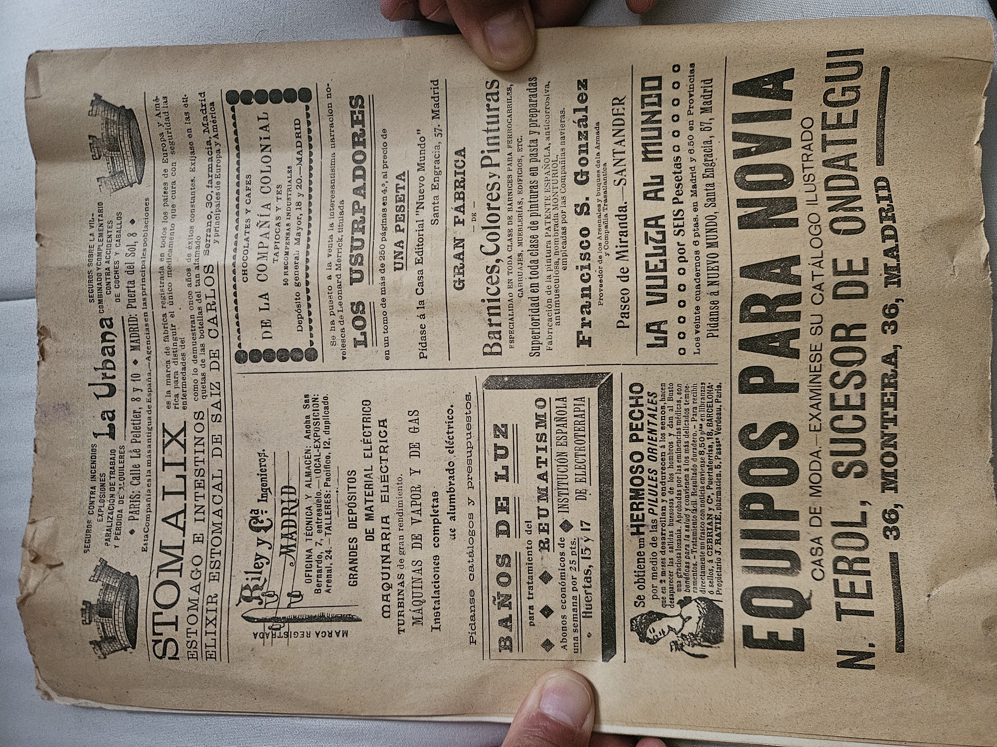 The image shows a fragment of an old newspaper advertisement, likely from the early 20th century in Spain. The text promotes various products and services, including "Stomalix" for stomach ailments, electrical supplies from Riley & Co, "Baños de Luz" (light baths) for rheumatism treatment, and "Pilules Orientales" for bust enhancement. The advertisement also features other businesses, such as "La Urbana" insurance, "Compañía Colonial" chocolates, and "Barnices, Colores y Pinturas" paint factory. A listing for "Equipos para Novia" (wedding outfits) highlights N. Terol, successor of Ondategui, located at 36 Montera Street in Madrid, indicating a fashion house.