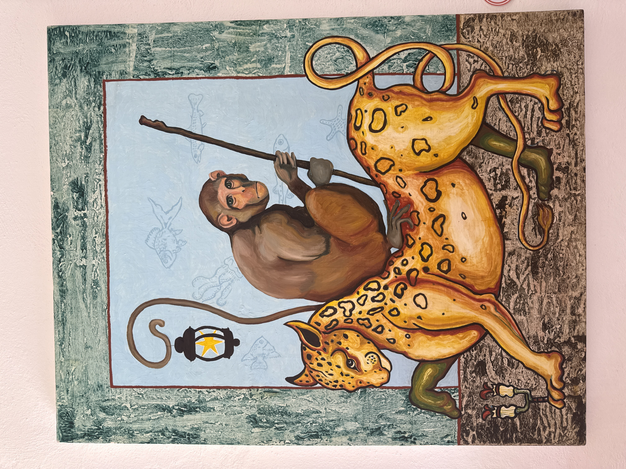 This painting, originating from San Andrés Cholula, Mexico, presents a vibrant and stylized scene featuring a monkey and a large feline creature. The artwork is composed of several distinct visual sections.
A brown monkey with light-colored skin on its face and green eyes is prominently featured on the left, gripping a dark brown stick horizontally. It appears to be suspended or swinging from the stick. The background behind the monkey is a light blue panel, subtly decorated with faint, translucent outlines of various marine life, including fish and starfish.
Dominating the right side and upper portion of the canvas is an elongated, yellow and orange leopard-like creature, covered in distinct black spots. This creature has a stylized form with multiple limbs and a long, looping tail. Its head, featuring a prominent snout and pointed ears, faces towards the bottom left. One of its forelegs extends towards the monkey's mid-section, while another leg is visible at the bottom right. Its tail forms intricate curls above its body and descends to the bottom left, where it culminates in a stylized black lantern with a yellow star emblem inside.
The light blue panel with the monkey is bordered by a textured, dark green frame that suggests an aged or weathered appearance. Beyond this green border, particularly on the right side, is a dark grey and brown textured panel, resembling tree bark or rough stone. At the bottom right, two red and green decorative elements, possibly resembling flowers or roots, are situated near one of the feline creature's legs. The overall style is illustrative and fantastical, blending elements of different environments within a single dynamic composition.