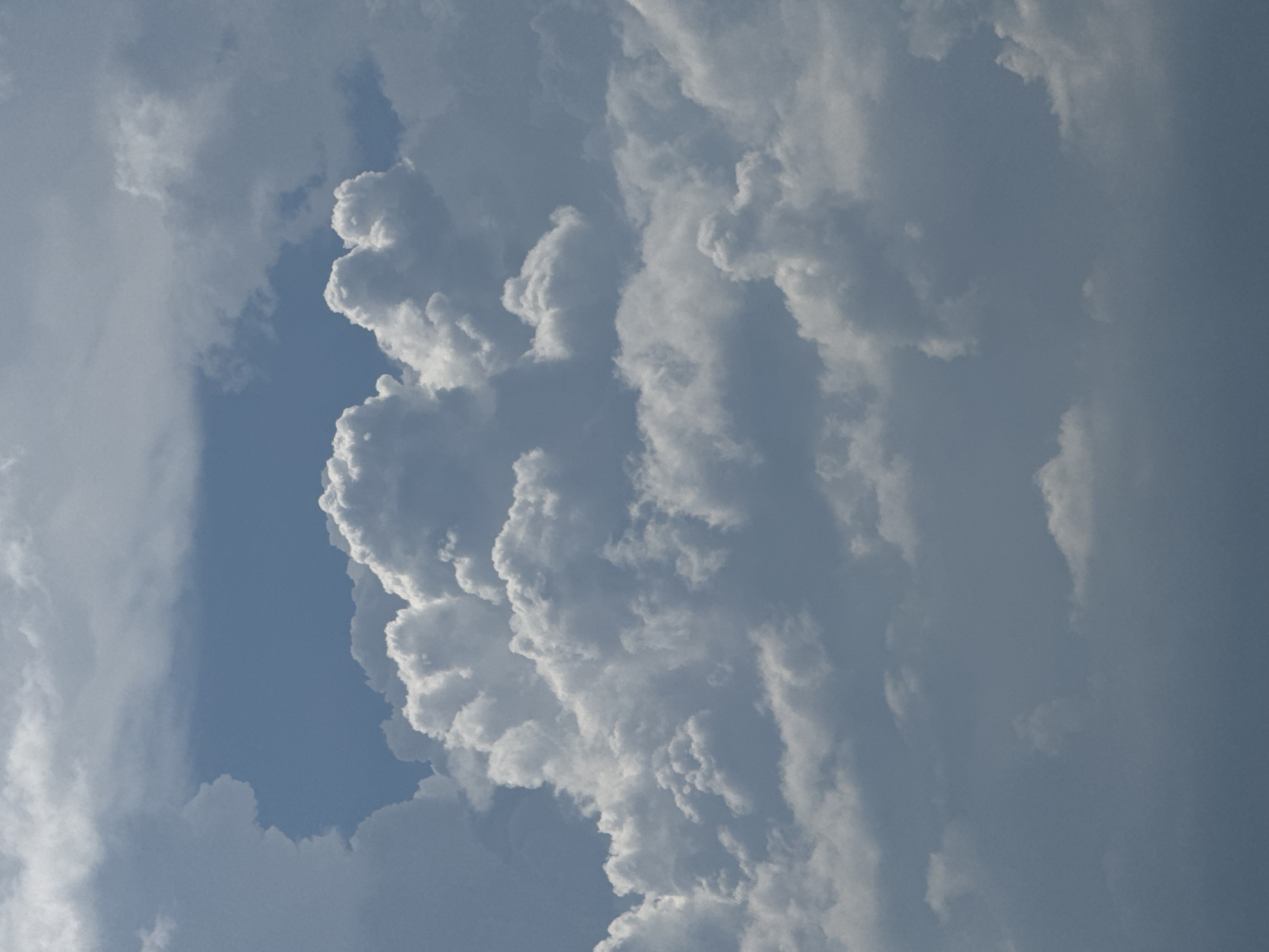 The image displays a cloudy sky with a patch of blue visible. The clouds are varied in texture and form, with some appearing dense and white, while others are more diffused and grey. The scene is likely outdoors. Without additional information or context, it is not possible to determine the location within Nha Trang Ward, Vietnam, or to identify any specific people, subjects, objects, or actions. The environment depicted is exclusively atmospheric.