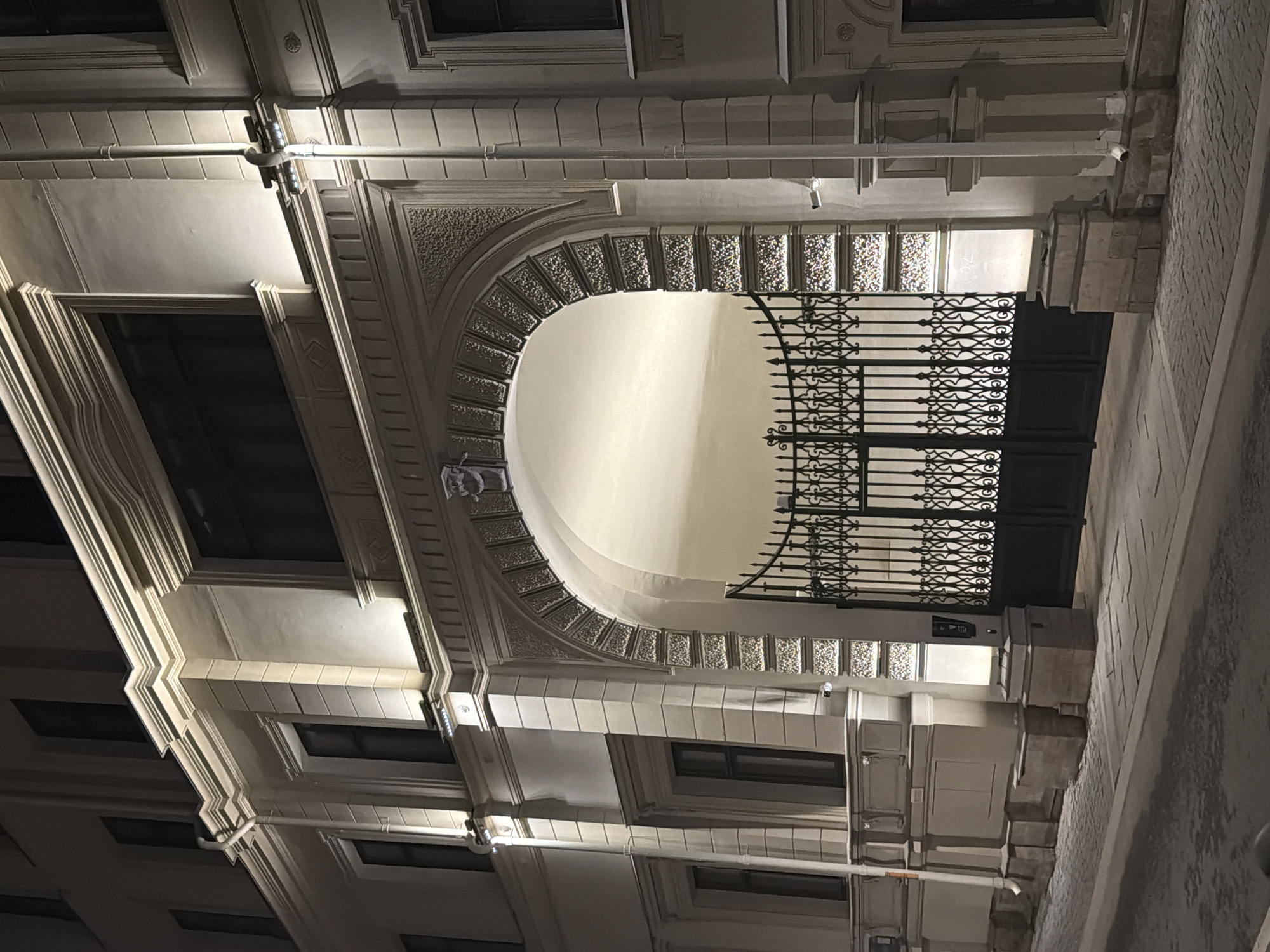 Captured at an angle, the image showcases an archway with a metal gate. The arch is ornamented with decorative molding. The building's facade is visible, exhibiting windows and architectural details. The setting appears to be outdoors at night, illuminated by artificial lights. The location is in Moscow, Russia.
