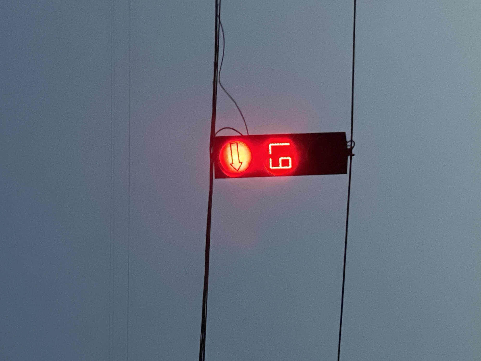 An outdoor, low-angle shot captures a traffic signal against a dusky sky in Ternopil, Ukraine. The signal is red, with a yellow left-pointing arrow illuminated above a digital display showing the number "67." The signal hangs from wires, and other wires are visible in the background, suggesting an urban or semi-urban setting. The overall lighting suggests it is either dawn or dusk. There are no people or vehicles visible in the frame.