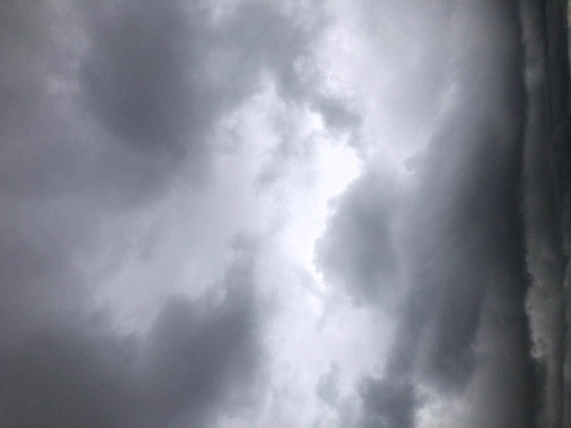 A cloudy sky fills the frame. The clouds are predominantly dark gray with some lighter, white patches visible. They appear thick and heavy, suggesting an overcast or stormy condition. The image is a full-frame shot of the sky, with no other elements of a cityscape or environment visible.