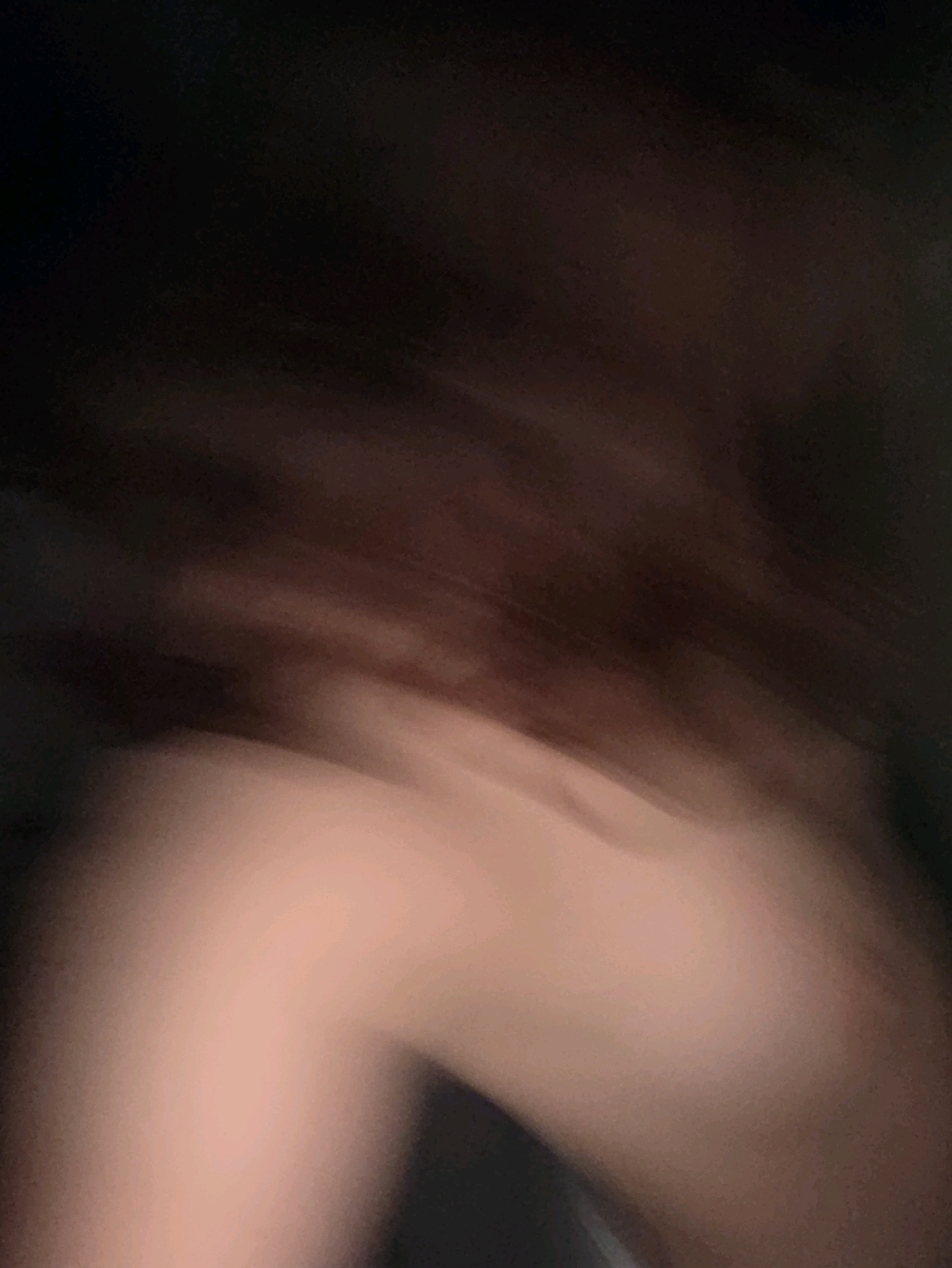 The image shows a blurry, abstract composition of skin tones and dark hair. The lighting is dim, creating a sense of shadow and depth. The texture of the skin appears smooth, with subtle variations in tone that suggest soft curves and contours. The dark hair is out of focus, creating a blurred background that contrasts with the lighter tones of the skin. It is not possible to determine the location within Phan Thiết, Vietnam, or any specific actions or interactions from this image.