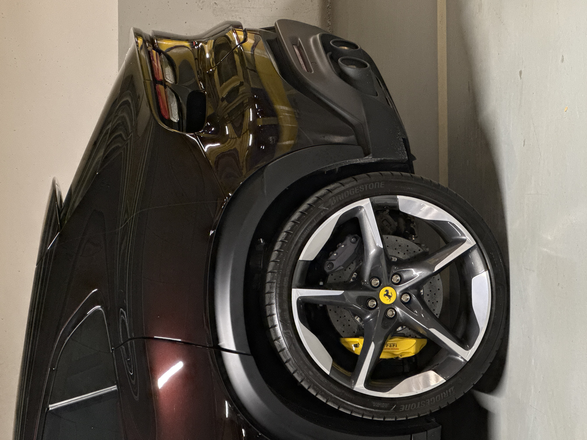 The image shows the rear portion of a maroon Ferrari, likely parked in an indoor garage. The tire is prominently displayed with the Bridgestone brand visible. The wheel features a five-pointed star design in gray and white, with a yellow Ferrari logo at the center. Yellow brake calipers are visible. The vehicle's bodywork is highly reflective. The background consists of a plain gray wall. The location in Sofia, Bulgaria is not directly discernible from the image.