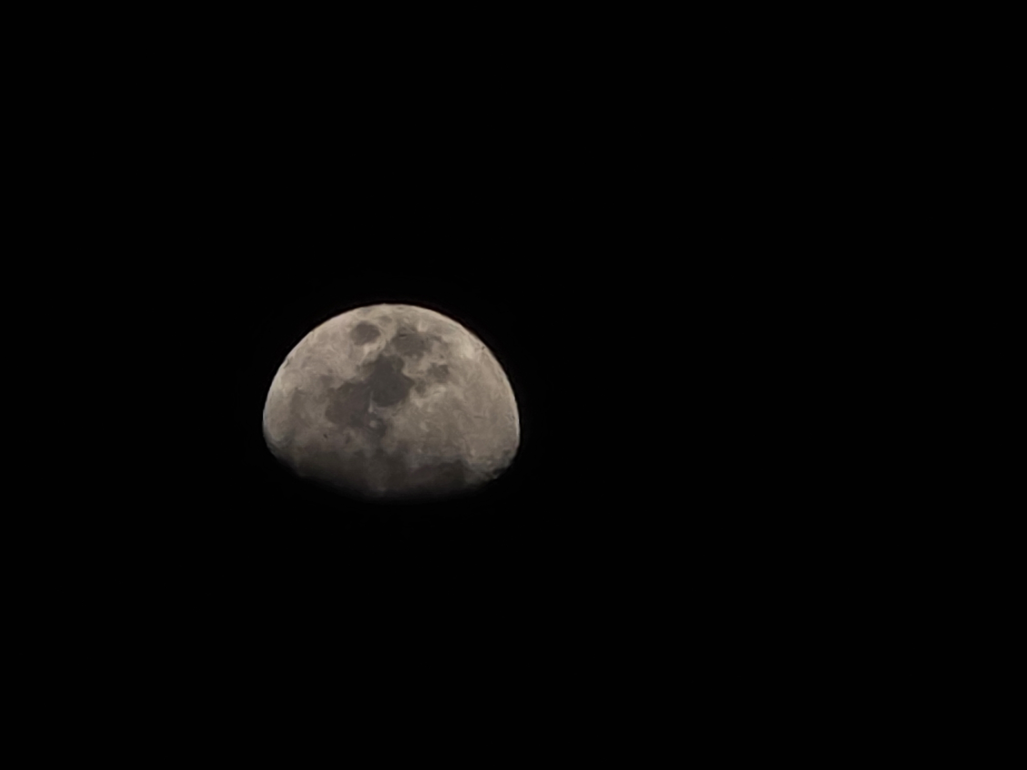 The media file shows a close-up of the moon against a black, starless sky. The moon is partially illuminated, revealing craters and a textured surface. It appears to be in the waning gibbous phase, with more than half of it lit. The lighting suggests it is nighttime. There are no people or man-made structures visible, and no text is present. The image captures the stark beauty of the moon in its celestial setting.