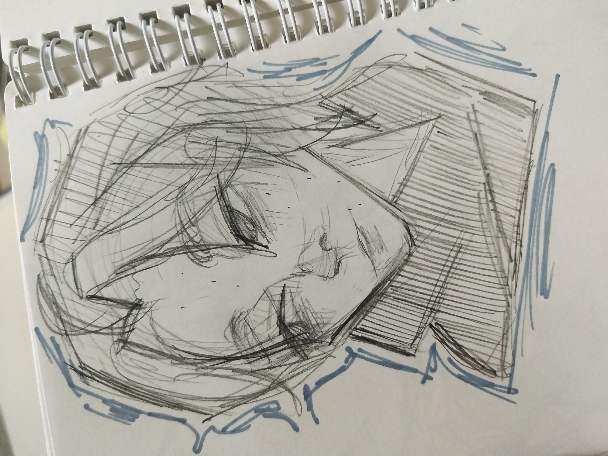 The image is a close-up sketch of an anime-style character's head and shoulders, drawn in a notebook with a spiral binding visible on the right side. The sketch is primarily in black and white, with some light blue accents used for shading or outline details around the character's hair and neck. The character has medium-length, layered hair with bangs. Their eyes are downcast and appear somewhat weary or melancholic, with dark shading around them. The nose and lips are softly rendered. The character is wearing a collared garment, indicated by vertical lines of shading on the chest area. The overall style is loose and sketch-like, with visible lines and scribbles suggesting quick work. There is no identifiable location in Gimhae-si, South Korea, or any elements that suggest a specific urban environment. The scene is limited to the drawing on the notebook page.
