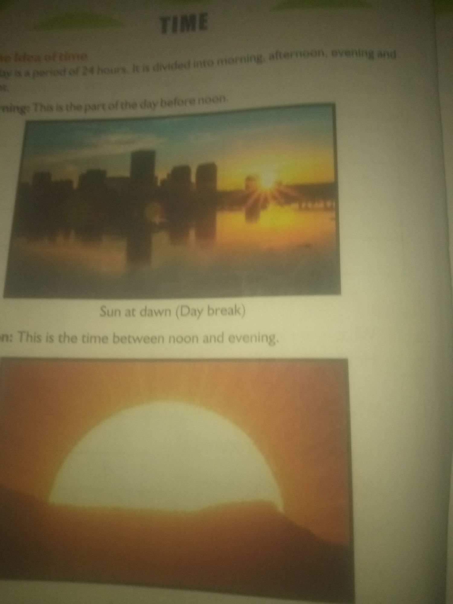 The image shows text and two photographs related to the concept of time. The first photograph depicts a city skyline at sunrise, with the sun's rays visible above the buildings. The text above this image labels it as "Sun at dawn (Day break)". The second photograph shows a close-up of the sun setting over a horizon, casting an orange glow. The text associated with this section describes time as being divided into morning, afternoon, evening, and night, and defines the morning as the period before noon. There is no information about the city of Jauro Yinu, Nigeria in this image.