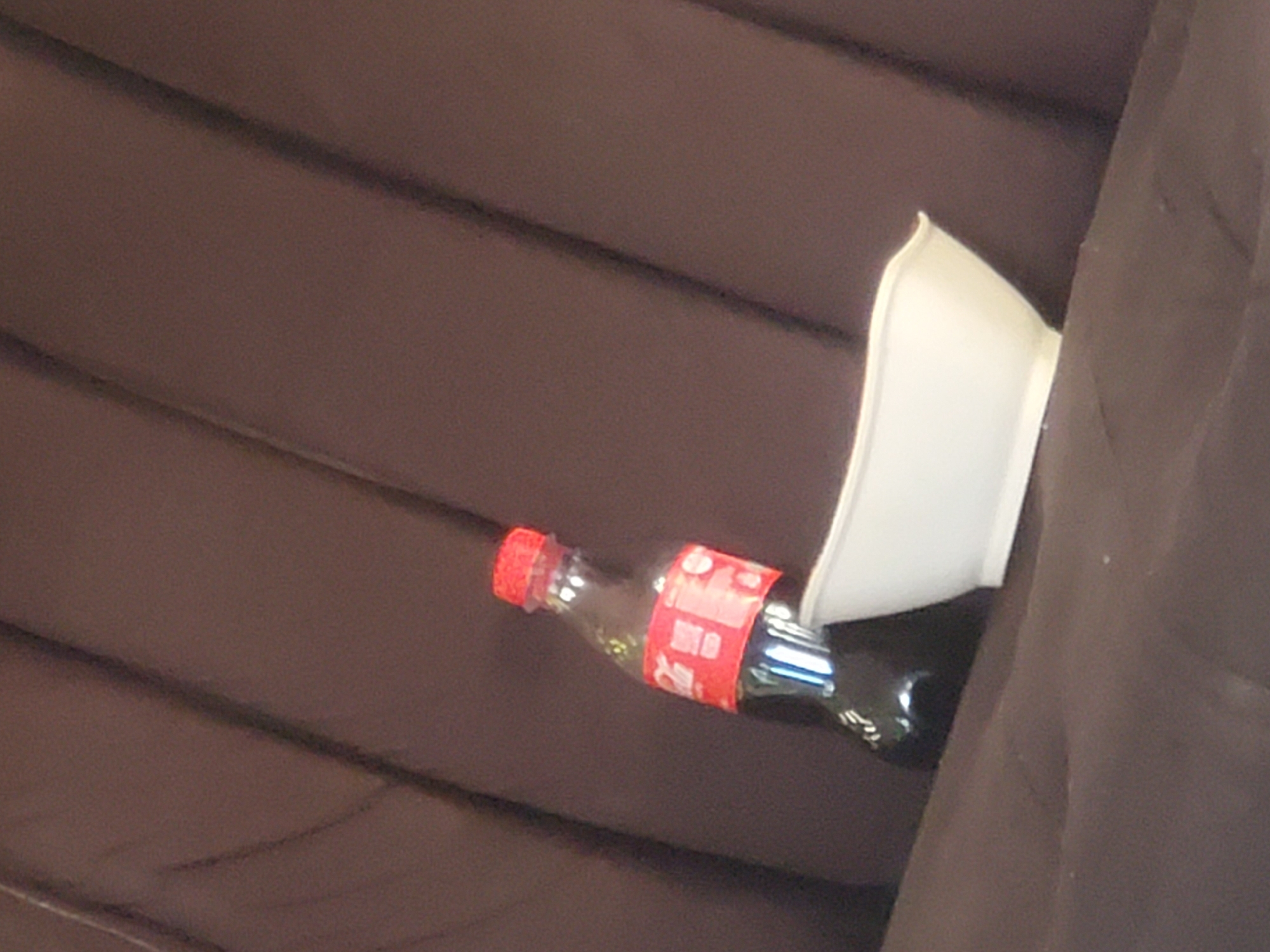 A Coca-Cola bottle lies on a dark brown surface next to a white bowl. The location, Rafin Bauna, Nigeria, is not inferable from the image.