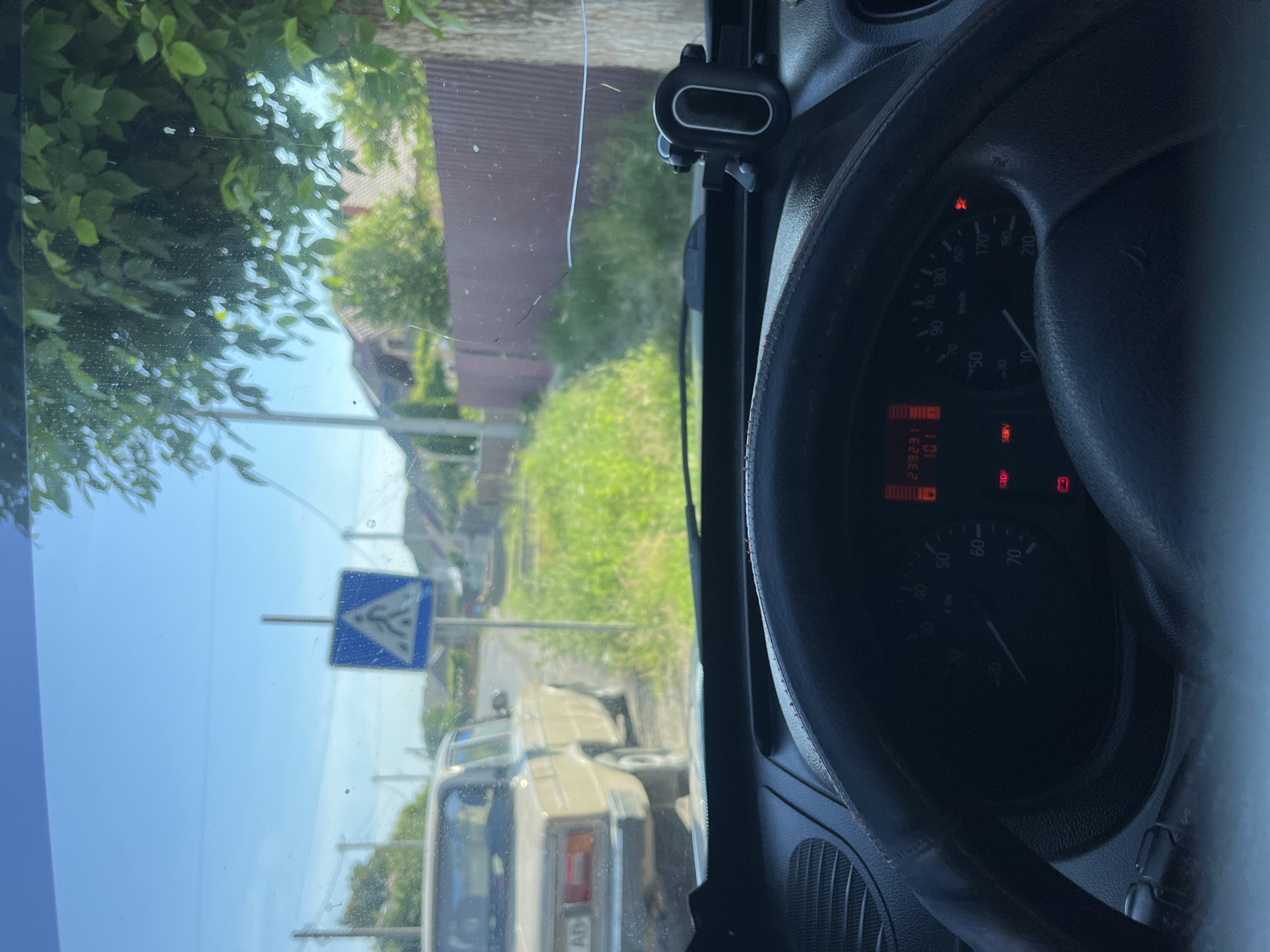 The image shows a view from the driver's seat of a car, looking through the windshield. The car is on a road in what appears to be a rural or suburban area, with houses and trees visible. A pedestrian crossing sign is prominently displayed on the right side of the road. The dashboard of the car is partially visible, showing the speedometer and other indicators. The weather appears to be clear and sunny. It is noted that this is a street view in Tarnivtsi, Ukraine.
