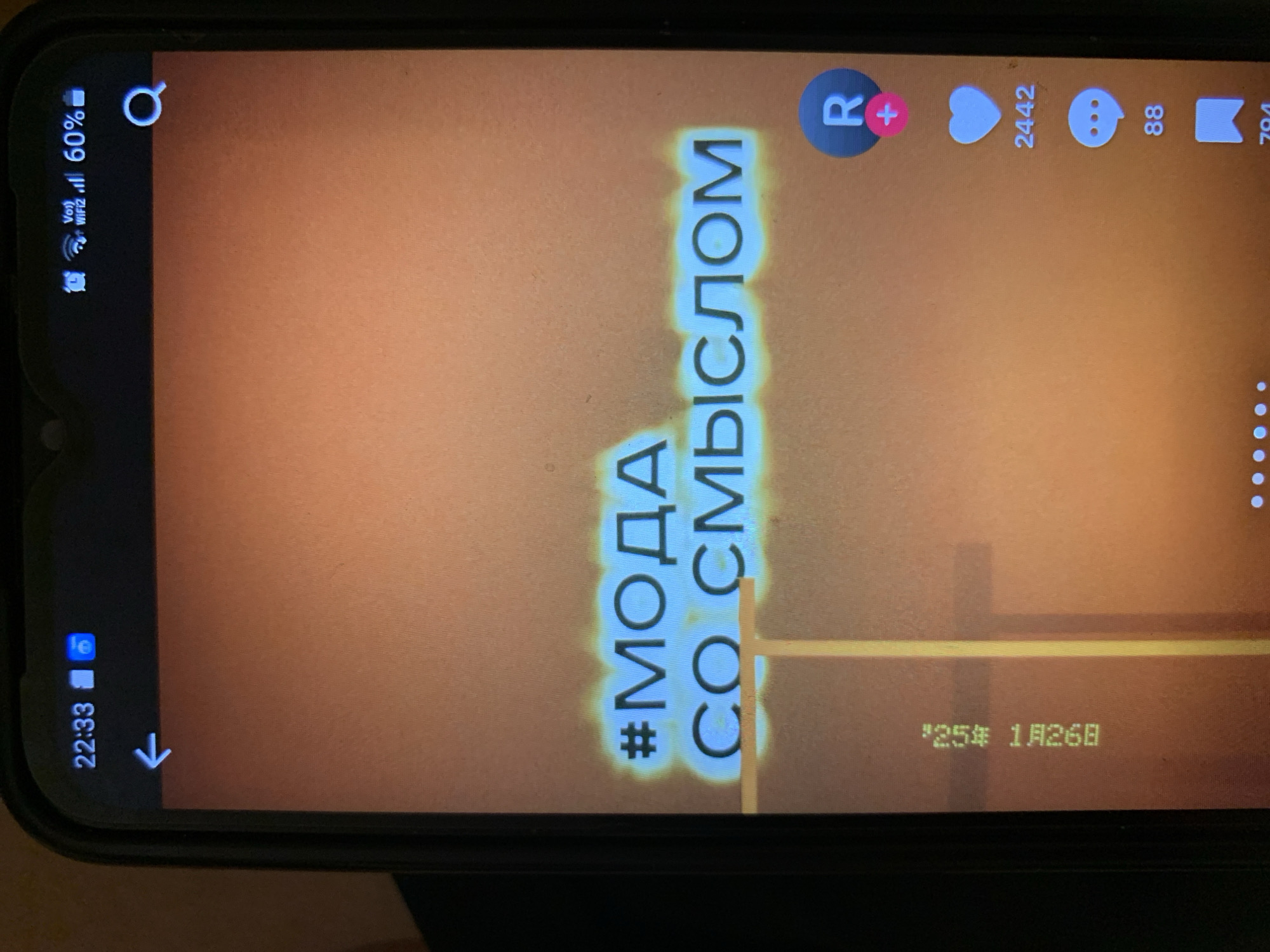 The image is a close-up of a smartphone screen displaying a social media video. The top of the screen shows the time "22:33", a battery icon, Wi-Fi signal, and "60%" battery percentage. A search icon is visible on the top right. The video content features the hashtags "#МОДА" and "СО СМЫСЛОМ" in large, glowing blue text on an orange, gradient background. On the right side of the screen, there are social media interaction icons: a circular profile icon with an "R" and a plus sign, a heart icon with the number "2442" below it, and a speech bubble icon with the number "88" below it. A bookmark icon is also visible at the bottom right. On the left side, there is a vertical string of green text that reads "1259 1A2G8". The image does not contain any information that could identify its location in the city of Lymanka, Ukraine.