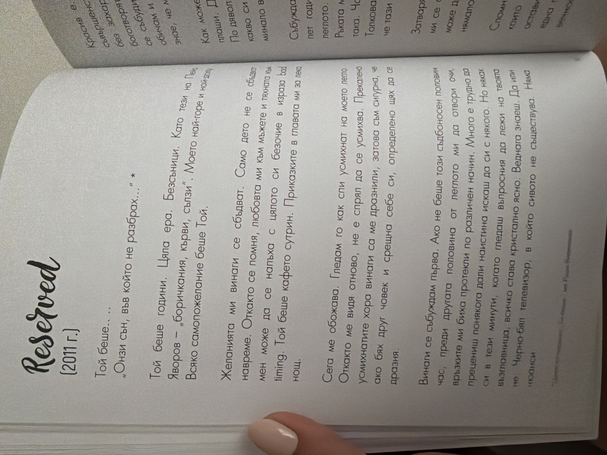 The image shows an open book with text in Bulgarian. The left page has a large cursive title "Reserved" followed by "(2011 г.)" in parentheses. Below this, there are several paragraphs of text. The right page also contains text, but it is partially obscured and appears to be in a smaller font size. The book is lying flat, and a person's hand with manicured nails is visible on the left side of the left page. The background is out of focus, suggesting a soft, indoor environment. There is no information in the image that links it to the city of Pazardzhik, Bulgaria.