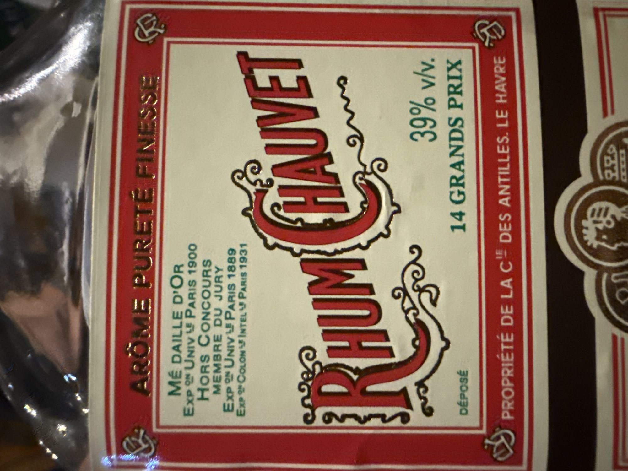 The image shows a bottle label with the words "RHUM CHAUVET" prominently displayed in a red, stylized font. Below this is "39% v/v" and "14 GRANDS PRIX." To the left, vertically aligned, is "AROME PURETÉ FINESSE," followed by a list of awards, including "MÉ DAILLE D'OR," "HORS CONCOURS," and "MEMBRE DU JURY," with references to the Universal Exhibition in Paris in 1900, 1889, and 1931. The label also states "PROPRIÉTÉ DE LA CIE DES ANTILLES. LE HAVRE." The label is primarily red, white, and gold, with decorative flourishes around the main text. The image does not provide information about the location in Mũi Né, Vietnam.