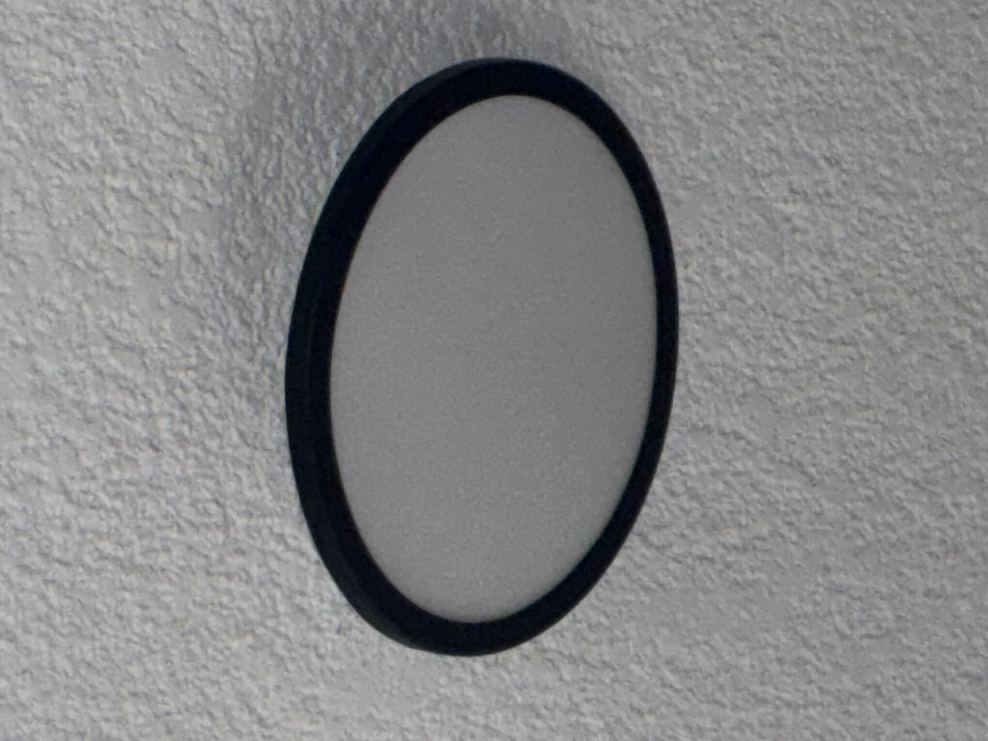 A close-up shot reveals an oval ceiling light fixture with a white center and a black rim against a textured, off-white ceiling. There is no information present in the image to determine the location.