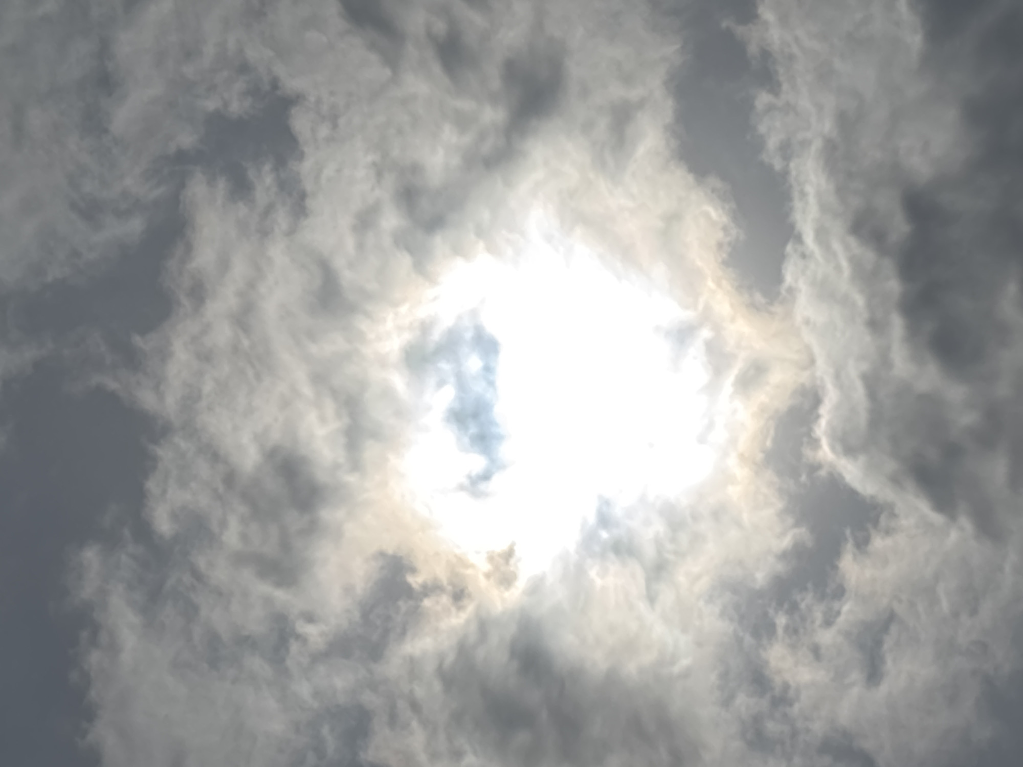 The image shows a view of the sky with clouds obscuring the sun. The clouds range in color from white to gray. The bright light of the sun is visible through a break in the clouds. The location is unspecified, making it impossible to confirm whether the location is in Burgas, Bulgaria.