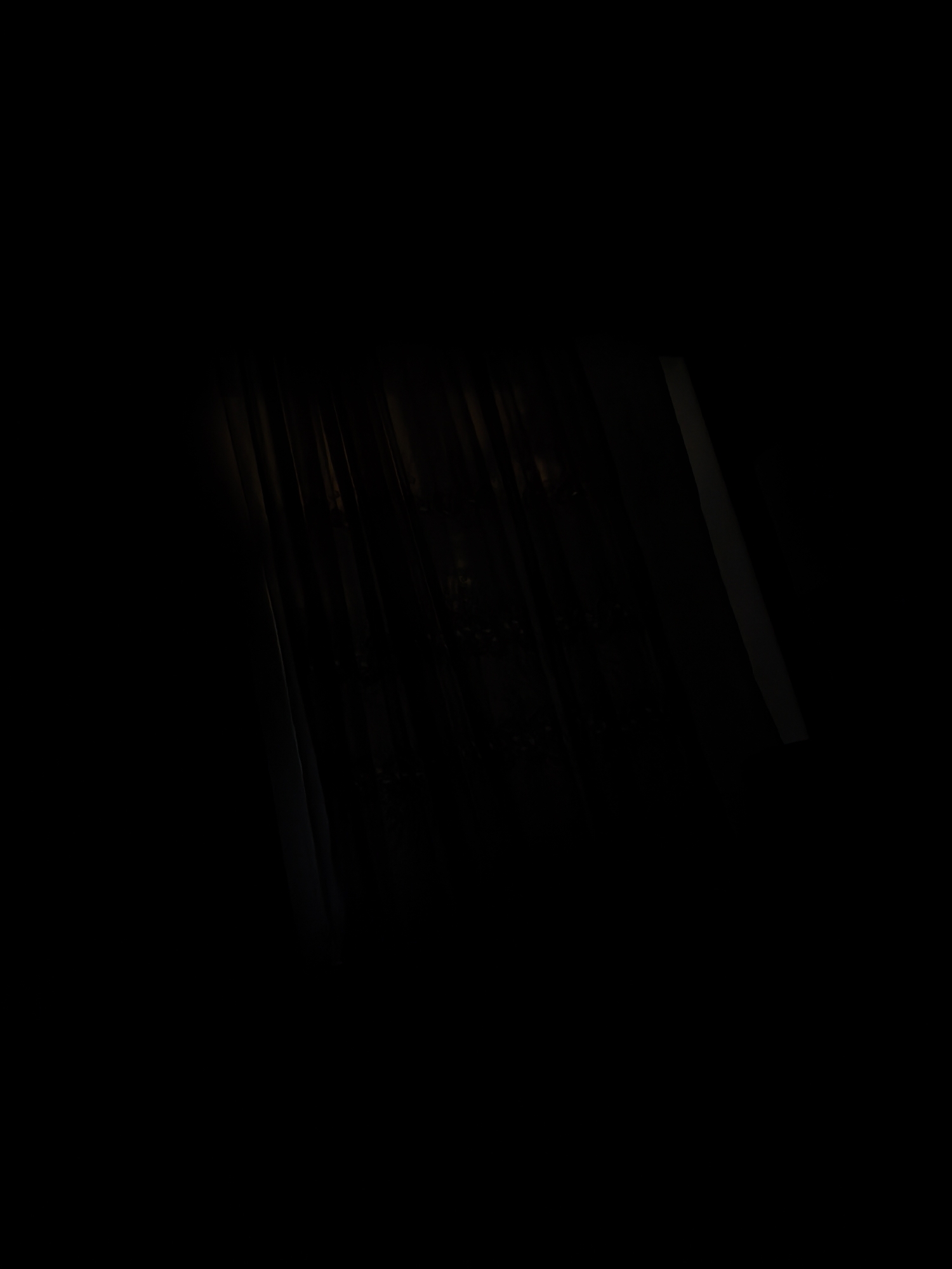 A dimly lit interior scene, likely a building, with dark walls and vertical lines suggesting wooden paneling or blinds. The lighting is minimal, creating a somber and possibly neglected atmosphere. The image does not contain any discernible people, objects, or actions that would indicate a specific location within Yeni Ramana Sabunçu, Azerbaijan, or any other city.