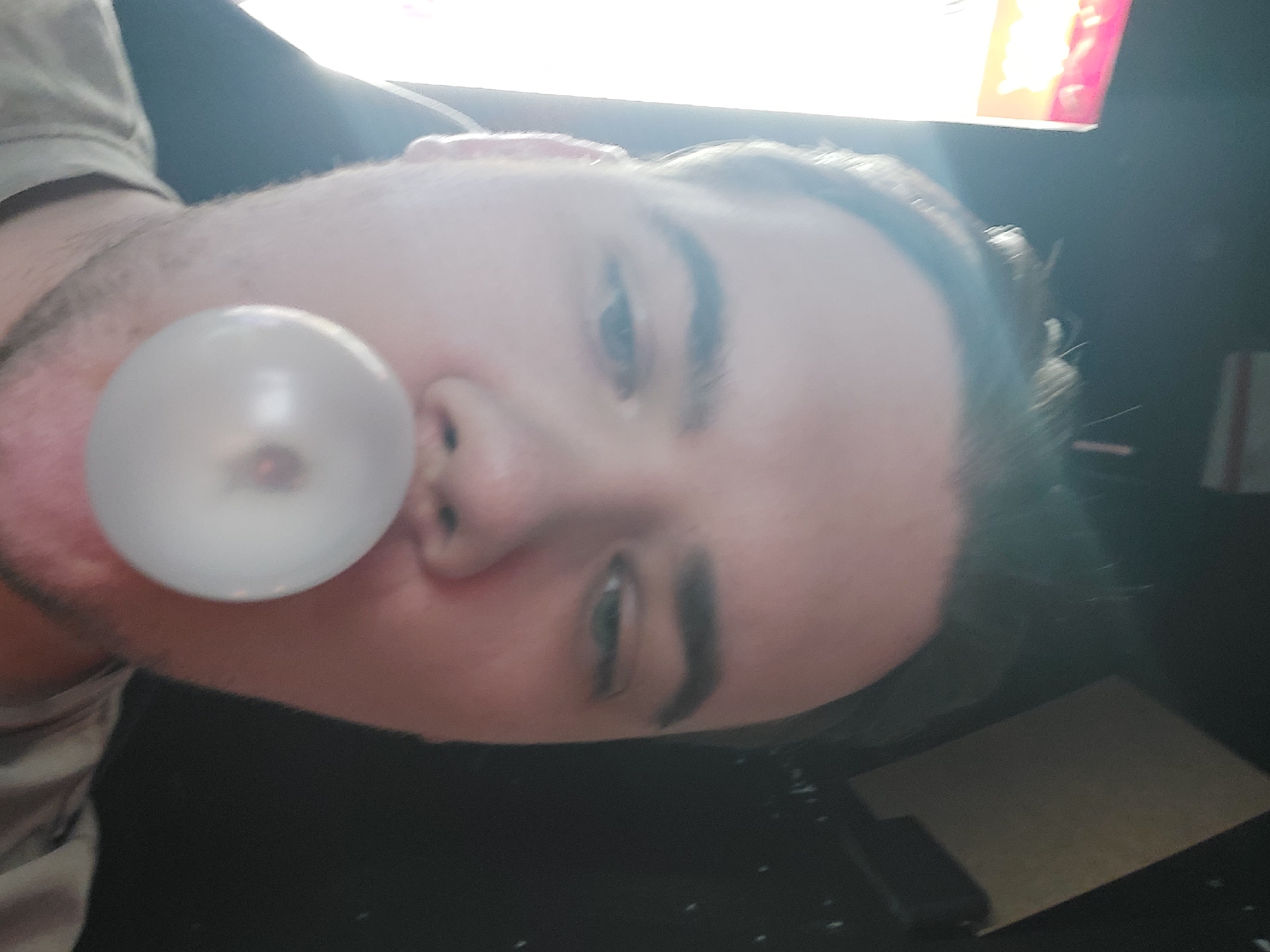 A person is inflating a bubblegum. The photograph appears to be taken indoors. There is a black surface visible below the person, possibly a table. There are no indications of the location being in Tashkent, Uzbekistan.