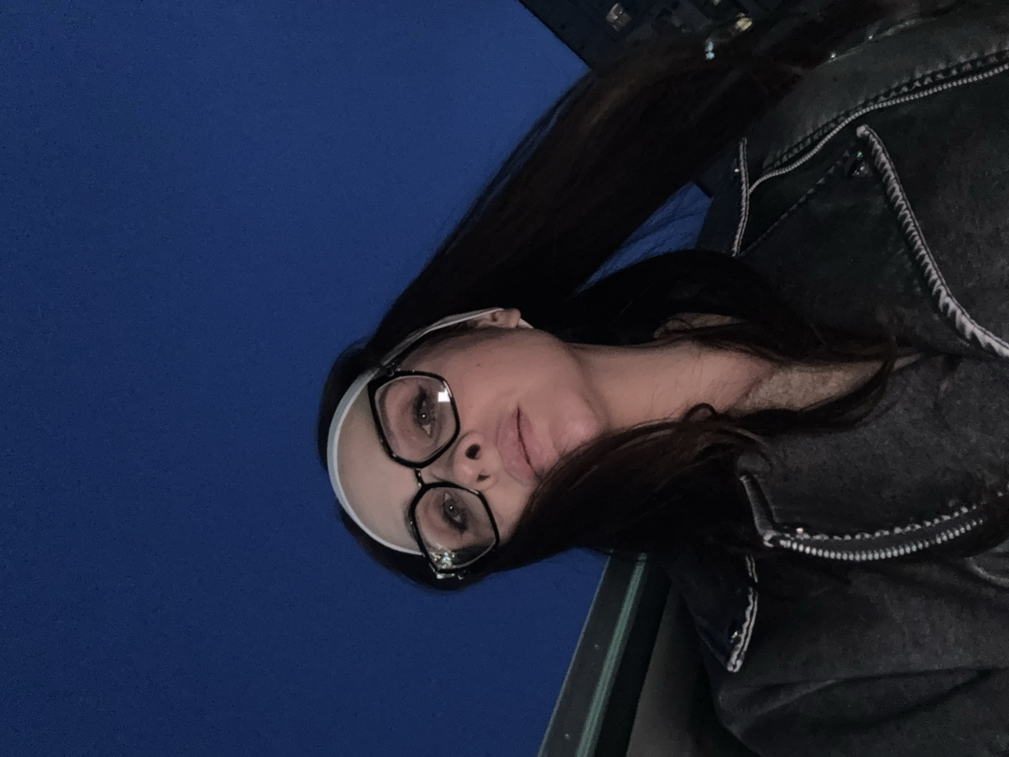 The image shows a woman wearing glasses, a white headband, and a dark jacket. The background is a dark blue sky. The location is likely outdoors at night, potentially in a city. There is no information in the image to suggest the location is Chaikovsky, Russia.