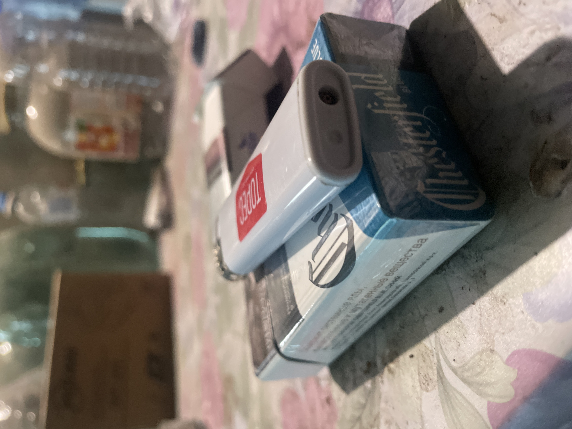 The image depicts a pack of Chesterfield cigarettes with a white lighter on top. The setting appears to be indoors, possibly a residence, in Olginka, Russia.