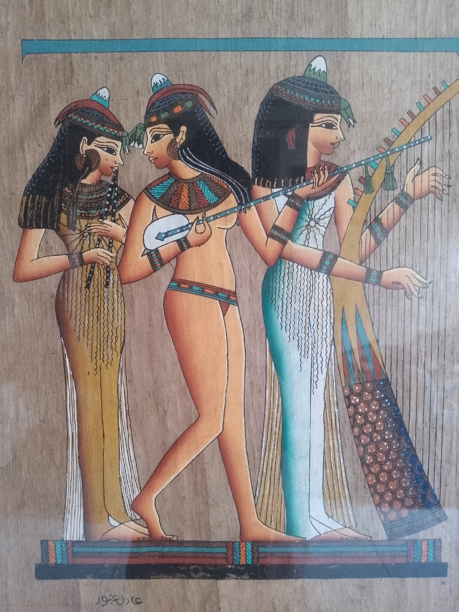 The image depicts three women in a style reminiscent of ancient Egyptian art. The figures are standing on a base with decorative horizontal bands.
From left to right:
Woman 1: Wearing a long, yellow dress with vertical lines, dark hair with a decorative headpiece, and jewelry around her neck. She is holding an object in her hands, possibly a musical instrument.
Woman 2: She is depicted with lighter skin, dark hair and headpiece, and wears minimal clothing - a decorative band around her neck and a loincloth or underwear. She is playing a white, lute-like instrument.
Woman 3: Dressed in a long, light blue or white gown, she also has dark hair with a decorative headpiece. She is playing a harp. The harp is decorated with colorful patterns, including red, blue, and brown elements.
There is a horizontal blue line above the figures. The background is a light-colored, wood-like surface. The image is likely a painting or reproduction of ancient Egyptian art. A signature is visible at the bottom left of the base.
There is no indication in the image itself that it is in Davao City, Philippines. Therefore, this location is not relevant to describing the content of the image.