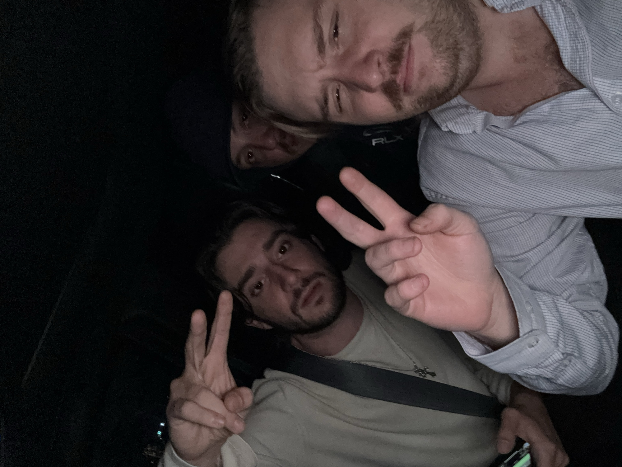 Three men are in a car at night. One man is in a light-colored shirt and seatbelt, holding a phone and making a peace sign. Another man wears a button-down shirt with a Ralph Lauren logo. Another man in a dark hoodie peeks from the back. Location: Huixquilucan de Degollado, Mexico.