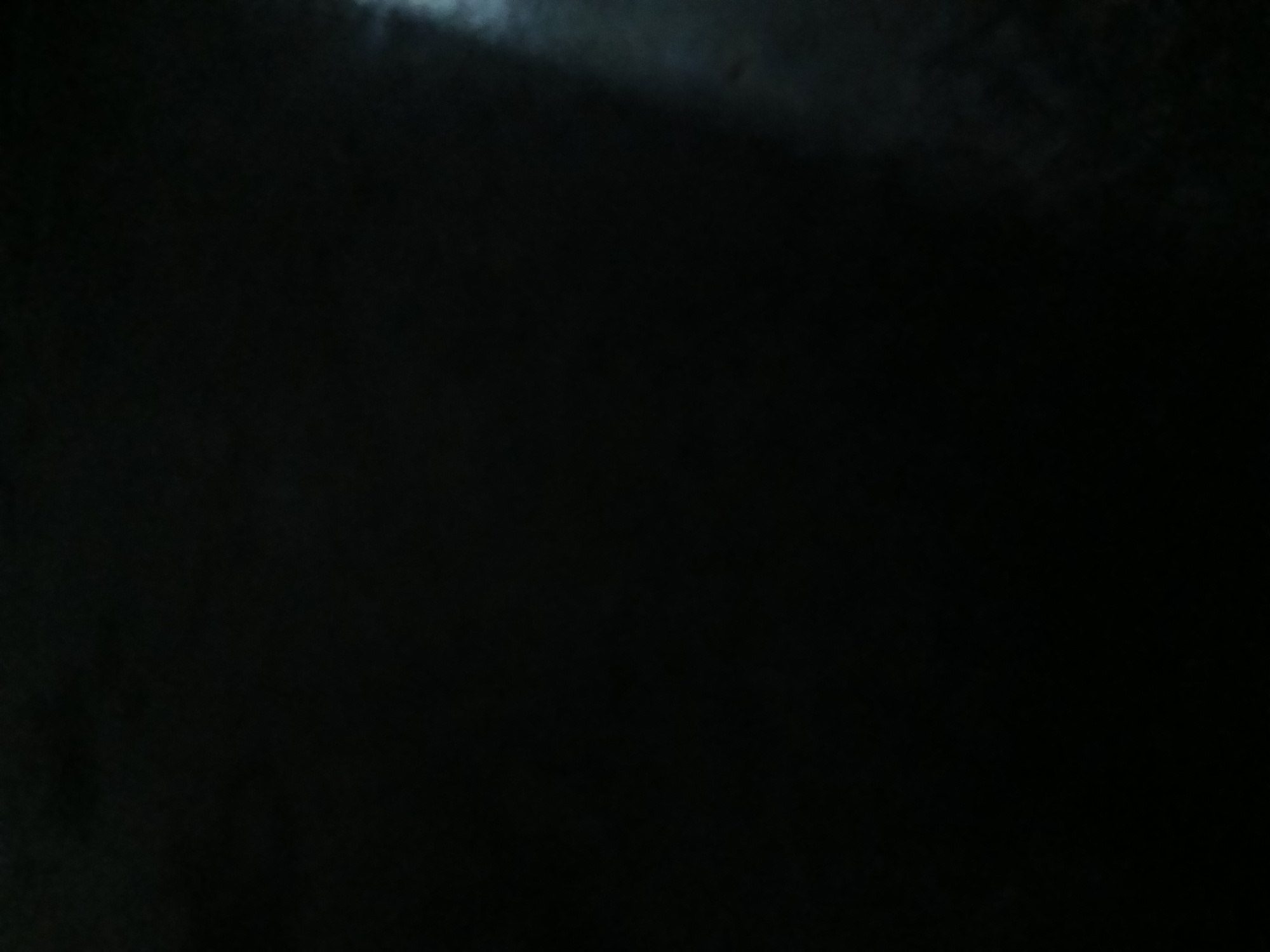 The image is a dark, grainy photograph of an indoor space. A faint light source is visible on the right side of the frame, illuminating a portion of what appears to be a floor or a dark, textured surface. No people, objects, or distinct features are discernible due to the low light conditions and poor image quality. The location in Kademangan Kulon, Indonesia, cannot be determined from the visual information provided.