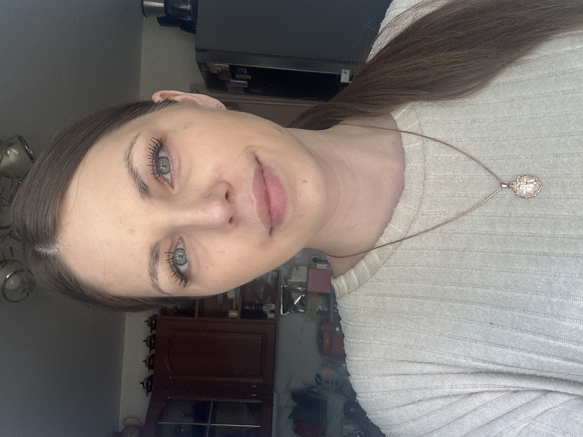 A woman is looking into the camera. She has blue eyes, and light brown hair. She is wearing a ribbed sweater. The location cannot be determined by the image.
