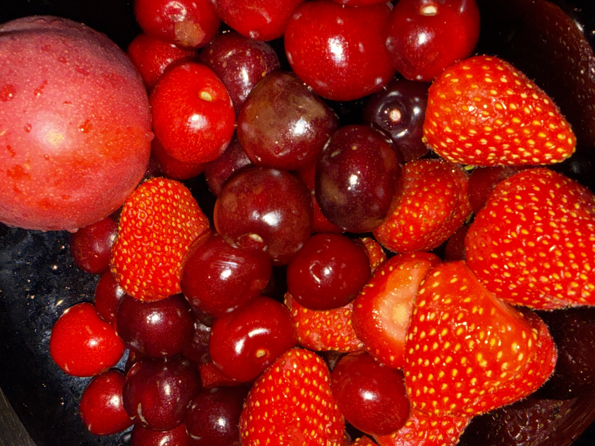 The image shows a close-up of a mix of fruits, including strawberries, cherries, grapes, and a plum. The fruits are clustered together in what appears to be a bowl, with some visible wetness suggesting they may have been recently washed. The color scheme is dominated by reds and purples. There is no information to suggest this image was taken in Sofia, Bulgaria.