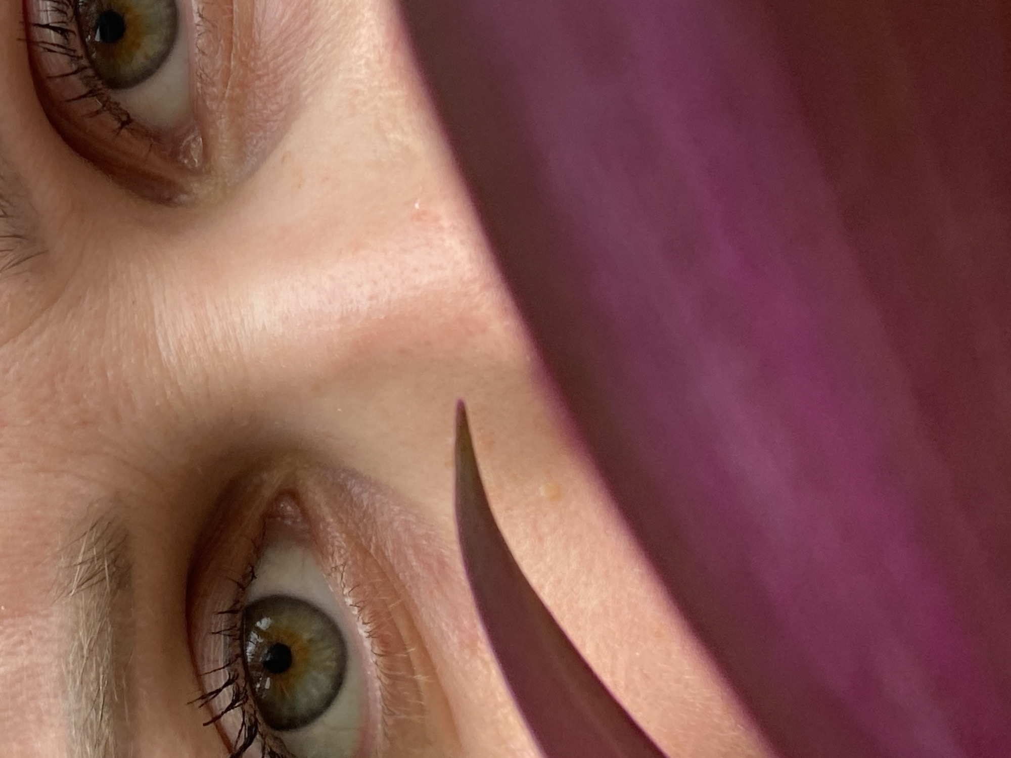 This close-up image shows a person's face rotated, with two eyes visible on the left side of the frame. The eyes are hazel-colored with dark eyelashes. The skin is light, showing fine wrinkles and a few small blemishes. A dark pink or purple object, possibly a petal or leaf, partially covers the right side of the face, casting shadows. The image has a shallow depth of field, focusing on the eyes and immediate surroundings. The location in the city of Марковский, Russia is not identifiable from the image content.