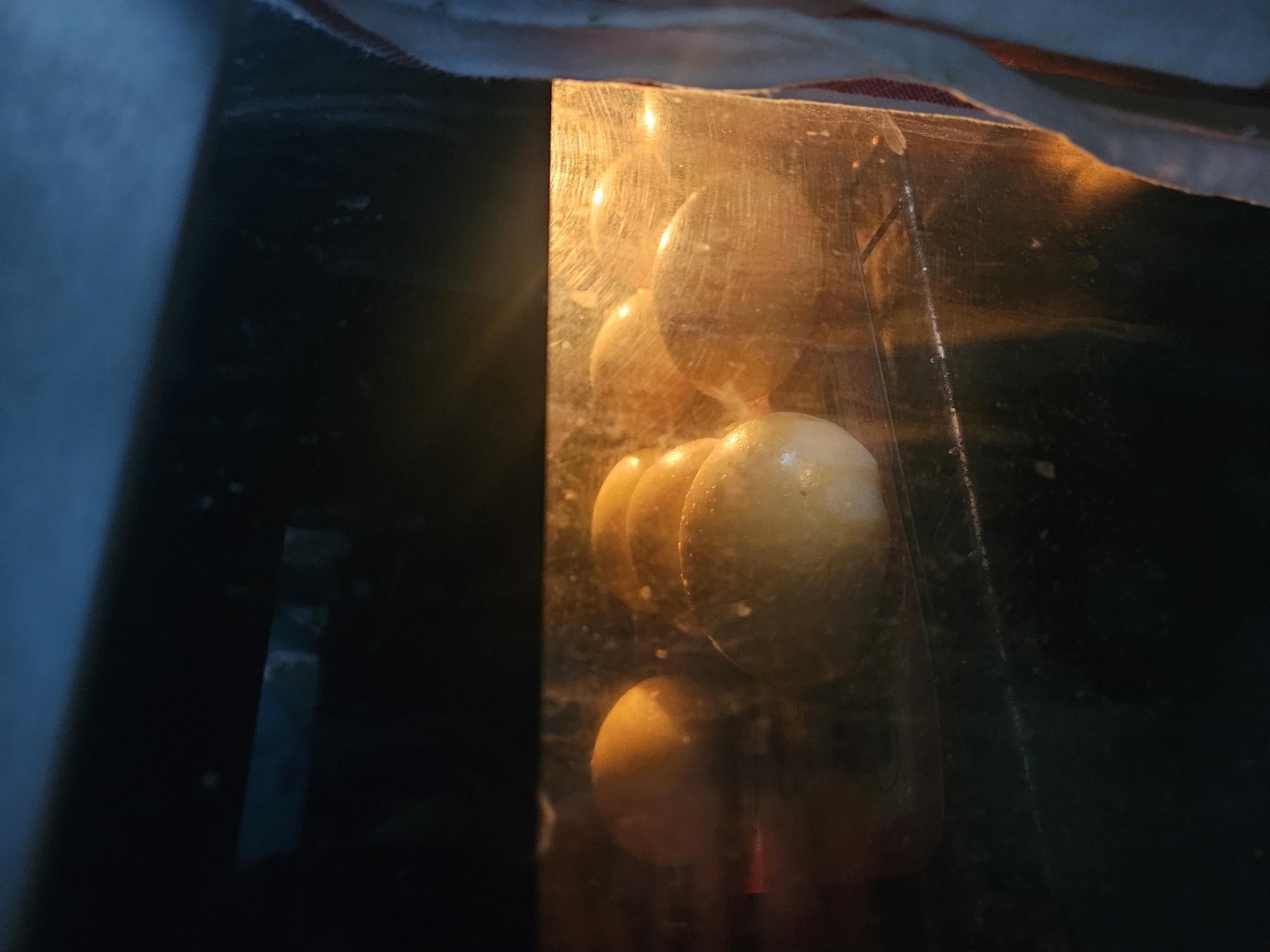 The image shows several orange spheres stacked vertically within a clear, rectangular container. The container sits in a dark space, possibly an oven or refrigerator, with light shining through the front. A piece of fabric is visible at the top of the frame. The location in Paris, France, cannot be determined from the visual information provided.