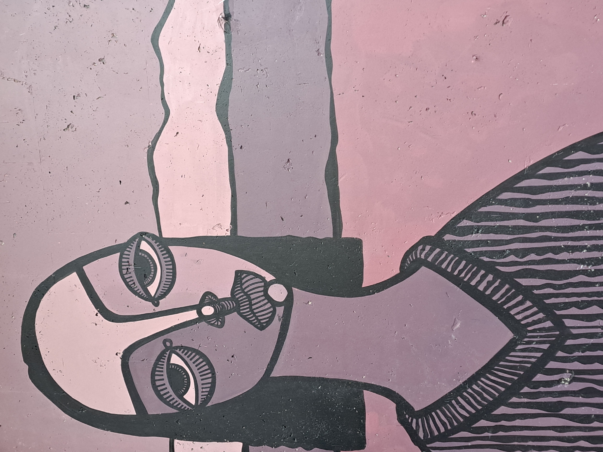 The image is a close-up of a mural-style painting, likely located in Yerevan, Armenia. The style of the painting is reminiscent of Picasso's cubism, featuring a reclining or laying down figure with a distorted face. The color scheme is primarily shades of pink, mauve, and gray, with black outlines. The painting is on a textured surface, which may be a wall or a concrete structure. The mural appears to be of a woman with a bottle on her head.