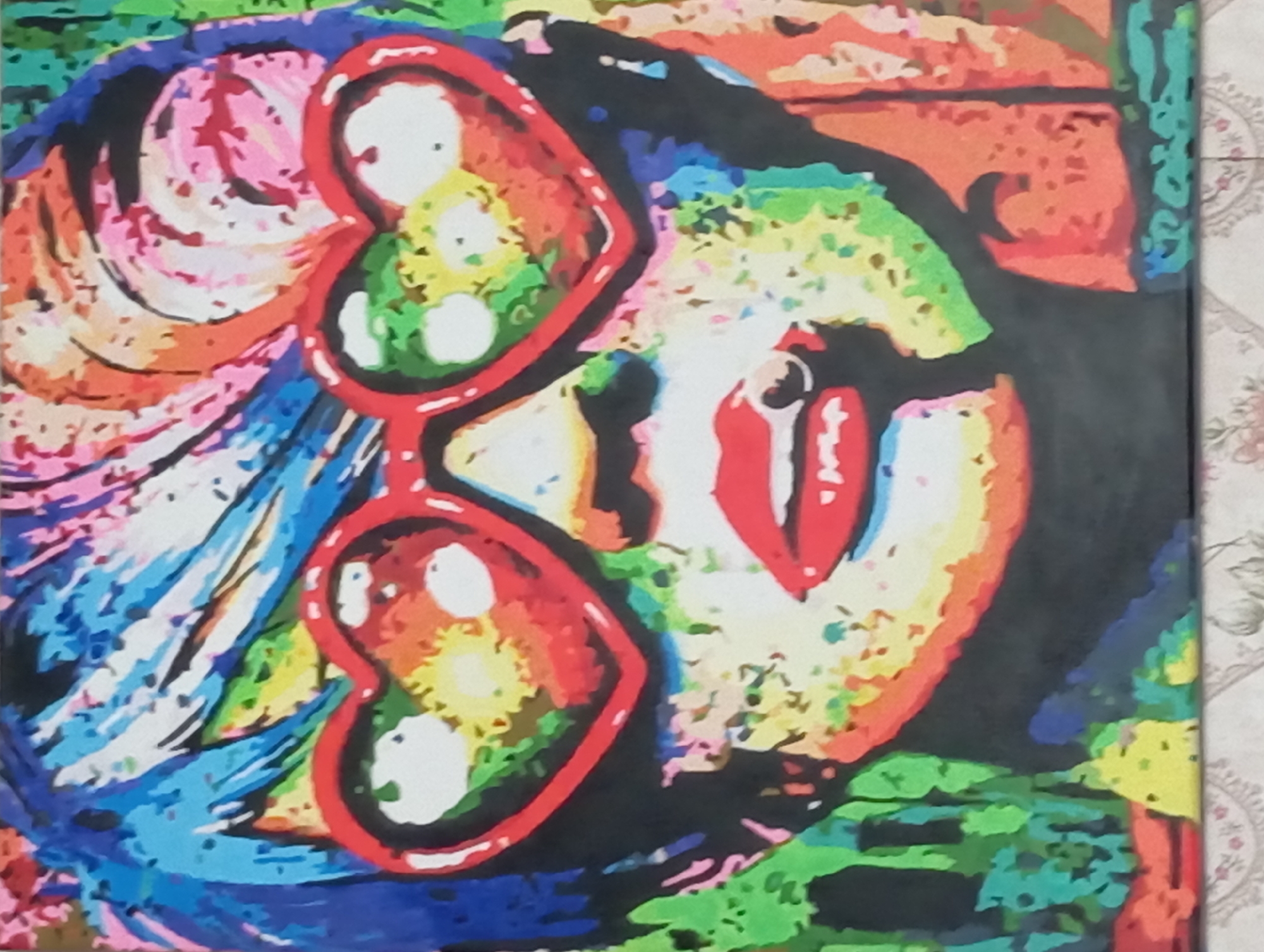 This is a vibrant, pop art style painting of a person's face, viewed in profile. The subject is wearing oversized heart-shaped sunglasses with red rims. The lenses of the sunglasses are filled with colorful swirls of yellow, green, and white. The person's lips are painted bright red and are slightly parted, revealing a glimpse of teeth. Their hair appears to be a riot of colors, with streaks of pink, blue, orange, and yellow. The background is a chaotic blend of various colors and shapes, suggesting a dynamic and energetic atmosphere. There are no visible text elements in the painting. The style is reminiscent of Andy Warhol's iconic portraits, with bold outlines and flat areas of color. The overall impression is one of playfulness and intense visual stimulation. The image does not provide specific cues about the time of day, weather, or a precise location beyond its artistic style.