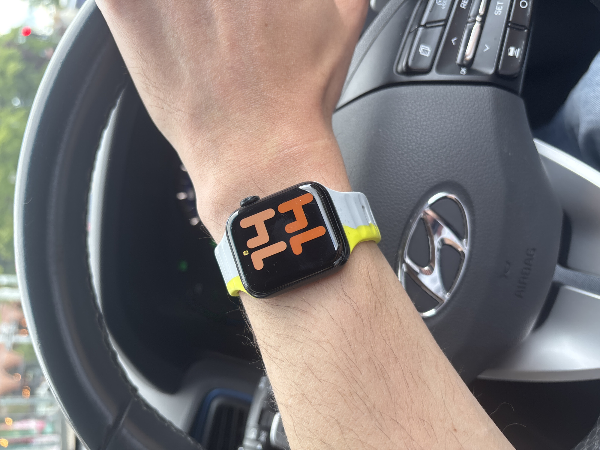 A person's arm is shown in the interior of a car, with an Apple Watch on the wrist. The watch face displays the time as 11:14 in orange numbers on a black background, and it has a two-tone grey and yellow band. The person's hand is resting on a black steering wheel featuring a silver Hyundai logo. The image was likely taken in daylight, though the precise location within Knutsford, United Kingdom is not discernible from the provided details.