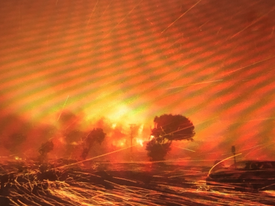 The image displays an event taking place in Kafr Sousa Municipality, Syria, dominated by intense orange and yellow illumination indicative of a large fire or explosion. On the left side of the frame, a dark, vertical structure is visible, from which numerous bright, linear streaks, consistent with sparks or incandescent debris, are actively ejecting diagonally upwards and to the right. Irregular, amorphous dark shapes are discernible within the bright orange and yellow glow, suggesting dense smoke or burning structural elements. No individuals are visible. The entire scene is engulfed in light and particulate matter, obscuring further specific environmental or structural details.