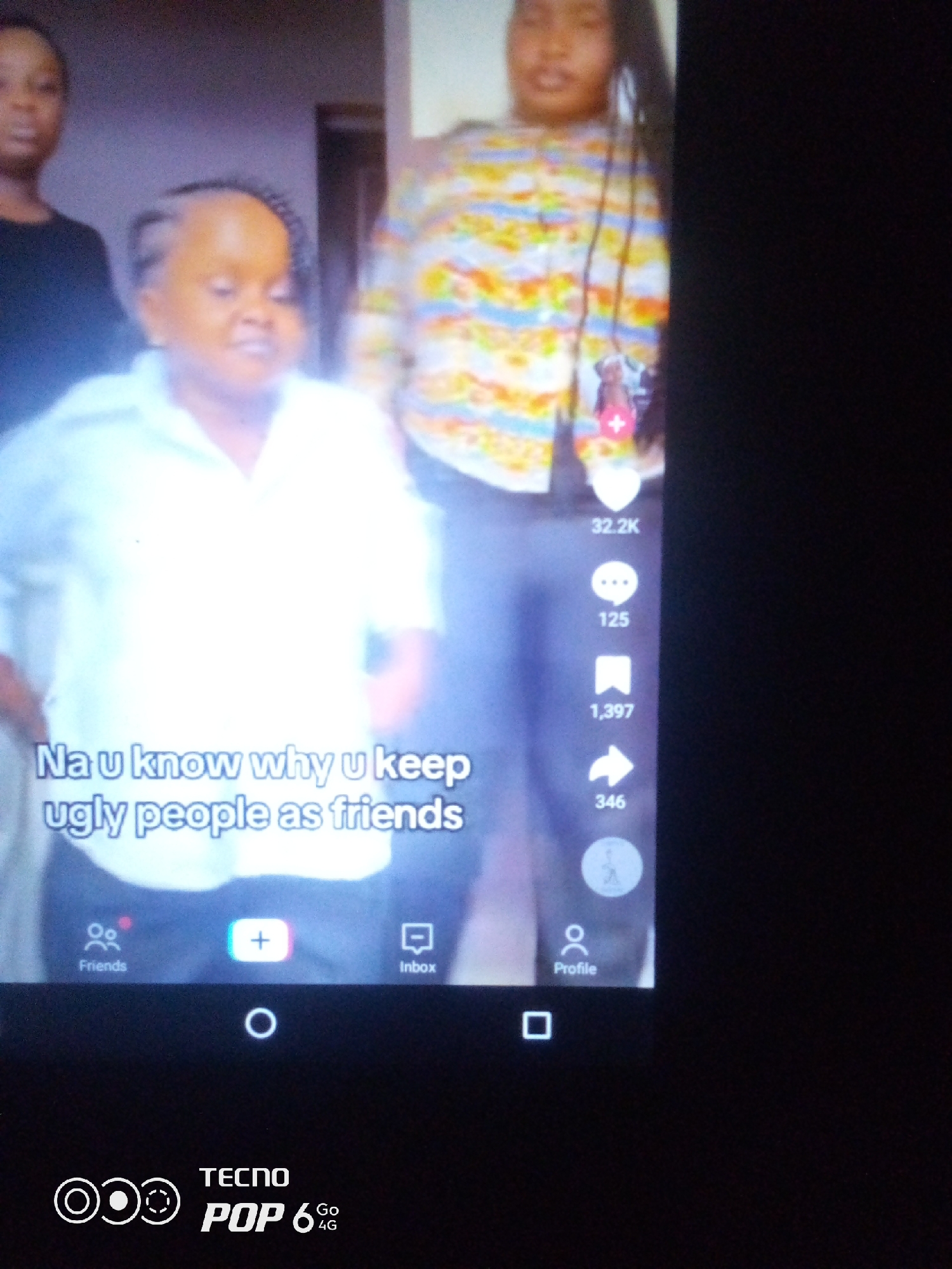The image shows a TikTok video being viewed on a Tecno Pop 6 4G smartphone. In the video, a person with a small stature and braided hair is wearing a white collared shirt. Behind them, two other people are partially visible. Text overlaid on the video reads "Na u know why u keep ugly people as friends". On the right side of the video, social media interaction icons and counts are displayed, including a heart with "32.2K" likes, a speech bubble with "125" comments, a bookmark with "1,397" shares, and an arrow with "346". At the bottom of the screen, navigation icons for "Friends," a "+" button, and "Inbox" are visible. The overall scene is a close-up of a smartphone screen displaying a social media video, with no discernable elements that indicate a specific location in Howayi, Nigeria, or any other city. The Tecno Pop 6 4G logo is visible at the bottom of the smartphone screen.