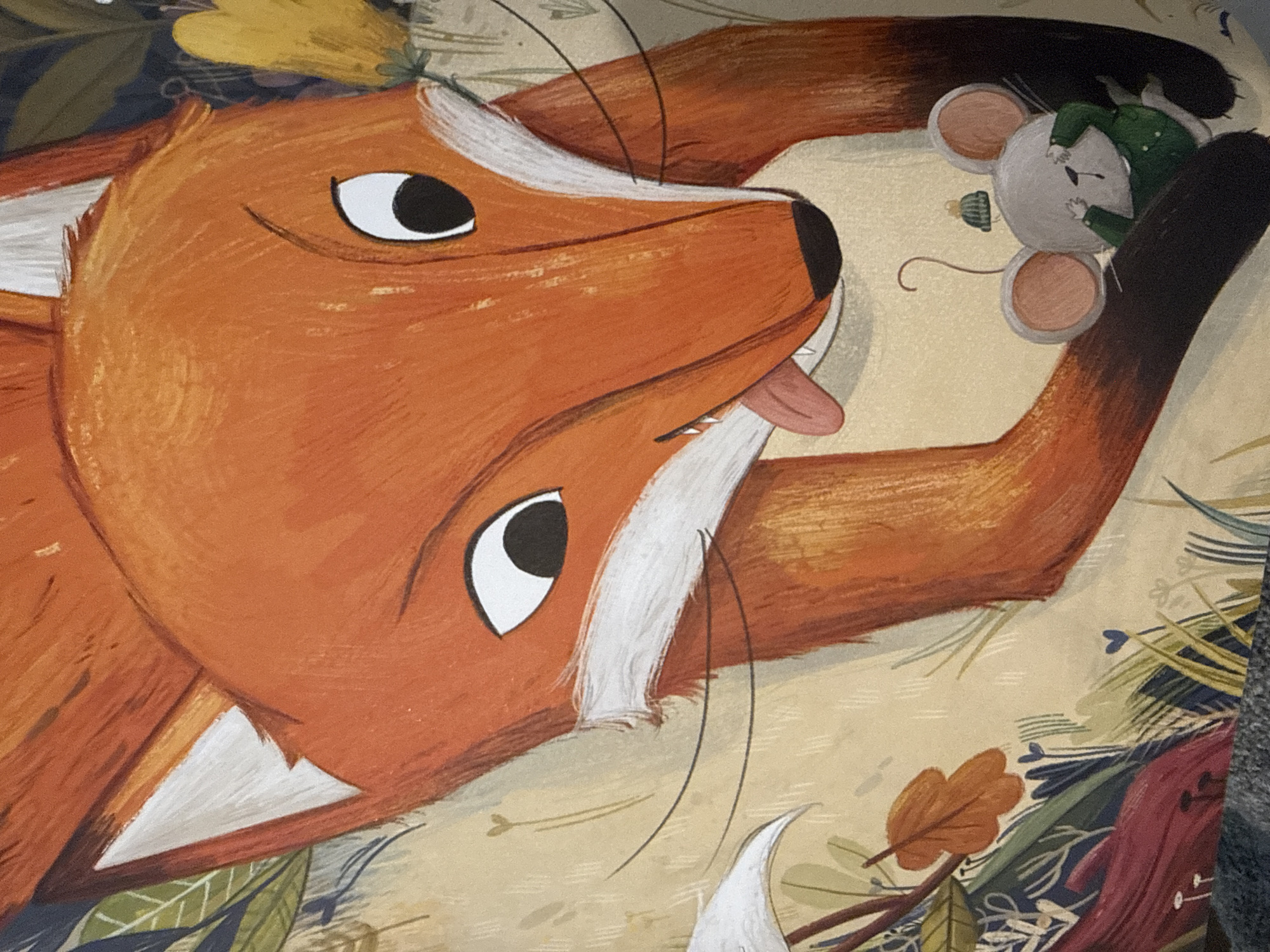 The image depicts a close-up illustration of a fox with bright orange fur and white markings around its muzzle and ears. Its tongue is sticking out. Below the fox, a small gray mouse wearing a green jacket and a knitted hat is partially visible, covering its eyes with its paws. The background features an artistic rendering of foliage with various green and dark leaves, as well as some yellow flowers. The image is a piece of artwork and does not depict a real-life scene in Dilijan, Armenia, or any other specific geographical location.