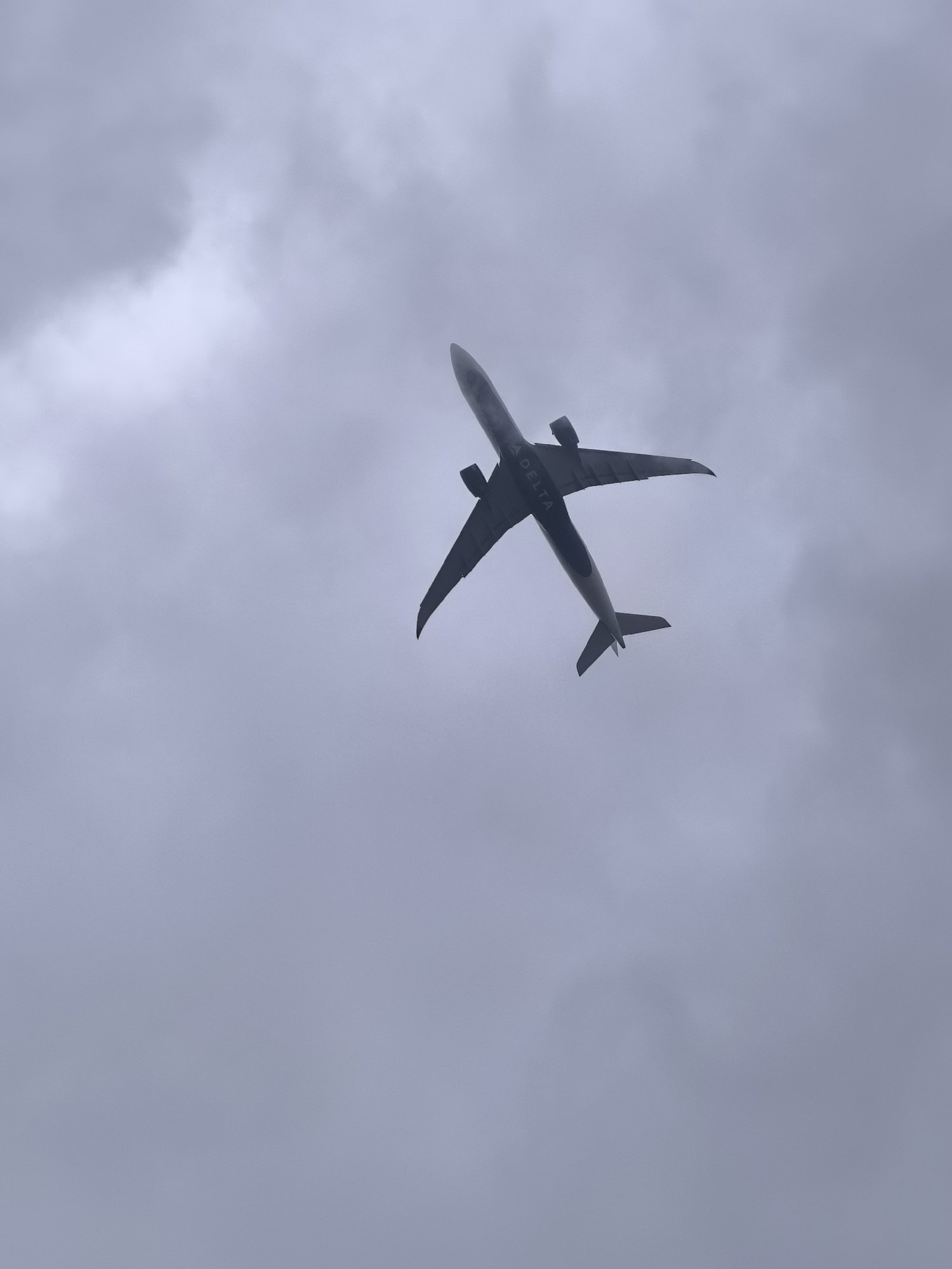 A Delta Air Lines passenger jet is flying overhead against a cloudy sky. The view is from below, looking up at the airplane. The location is not specified as Castricum, Netherlands in the image.