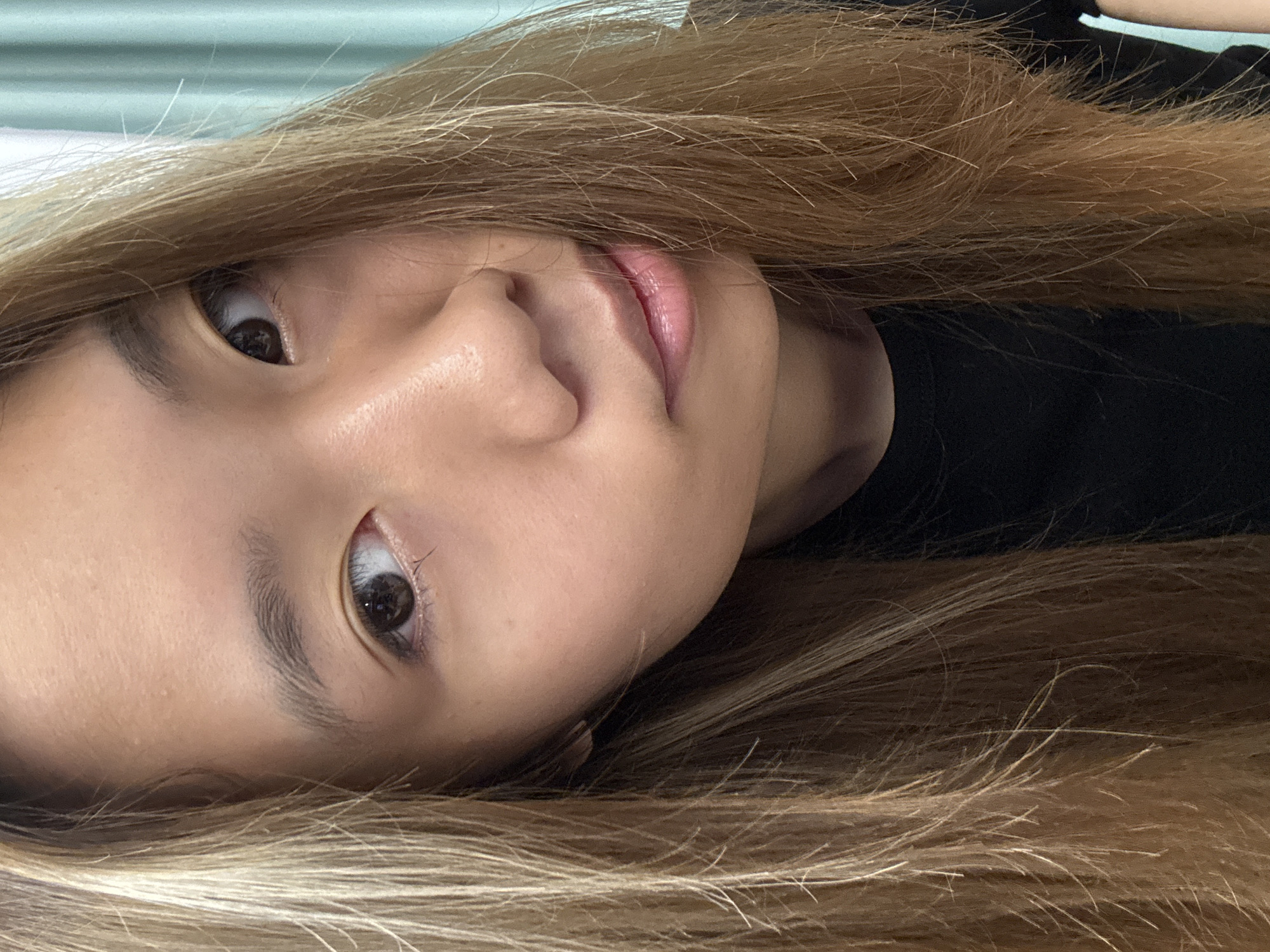 A close-up, angled portrait of a young woman with light brown hair. Her face is positioned slightly off-center, with her eyes open and directed toward the viewer. Her skin tone is fair, and her lips are slightly parted. She appears to be wearing a dark-colored top. The background is out of focus, suggesting a soft or diffused light. There is no indication of the location being in Nan'an District, China, as no contextual clues are present.