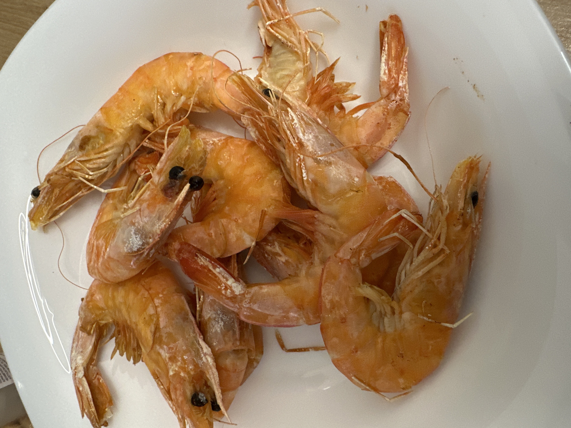 A close-up overhead shot shows a pile of cooked shrimp on a white plate. The shrimp are orange in color with visible shells, legs, and antennae. Black dots represent the eyes. The background is slightly out of focus. There's no evidence to associate this image with the city of Sofia, Bulgaria.